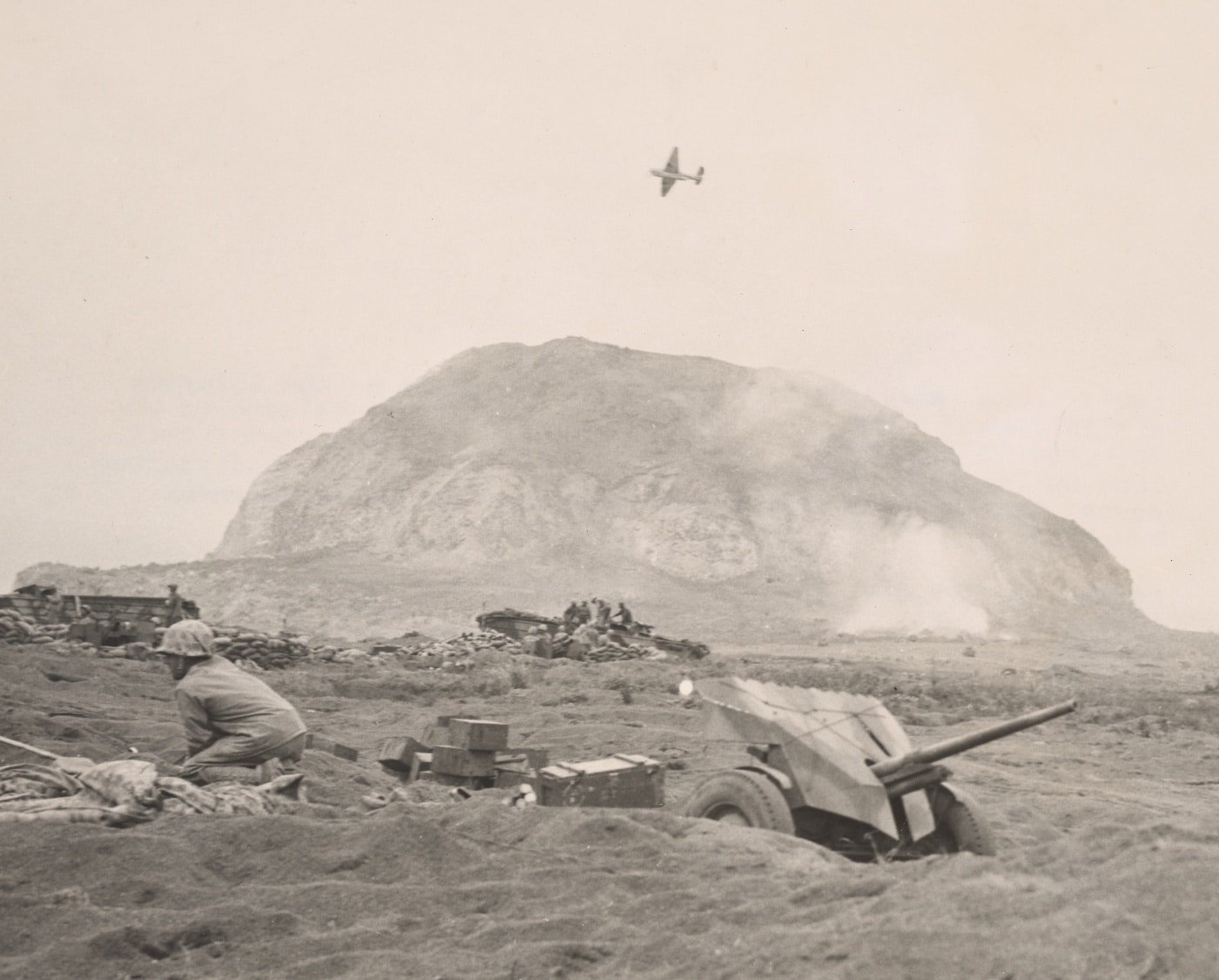 In this photo, a U.S. fighter flies over Mt. Suribachi. This was part of the Bonin Islands campaign in military history. In the Battle for Iwo Jima lasted until the end of the battle in the black volcanic sand that the 4th and 5th Marine Divisions had to slog through to achieve victory at Iwo Jima. 