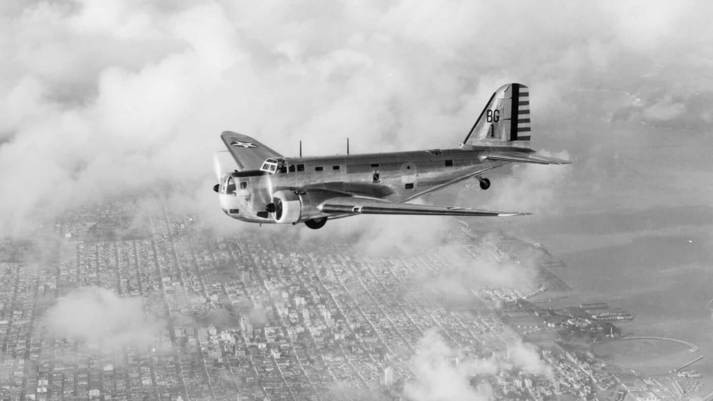 In this photograph, we see a Douglas B-18 Bolo flying from right to left over San Francisco, a city in California. The bomber has the brightly polished aluminum finish (silver colored) and not an olive drab or camouflage pattern that will be common when the United States of America enters World War II. A bomber is a military combat aircraft air-to-ground weaponry, launching torpedoes, or deploying air-launched cruise missiles. The first use of bombs dropped from an aircraft occurred in the Italo-Turkish War.