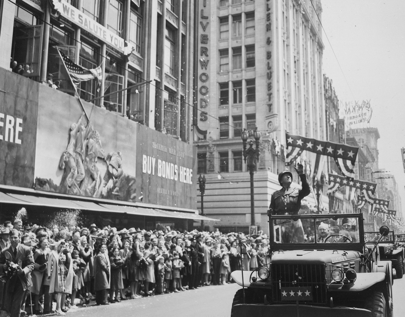 In this photo, we see Gen. Patton waving to a crowd while he rides by in a parade.