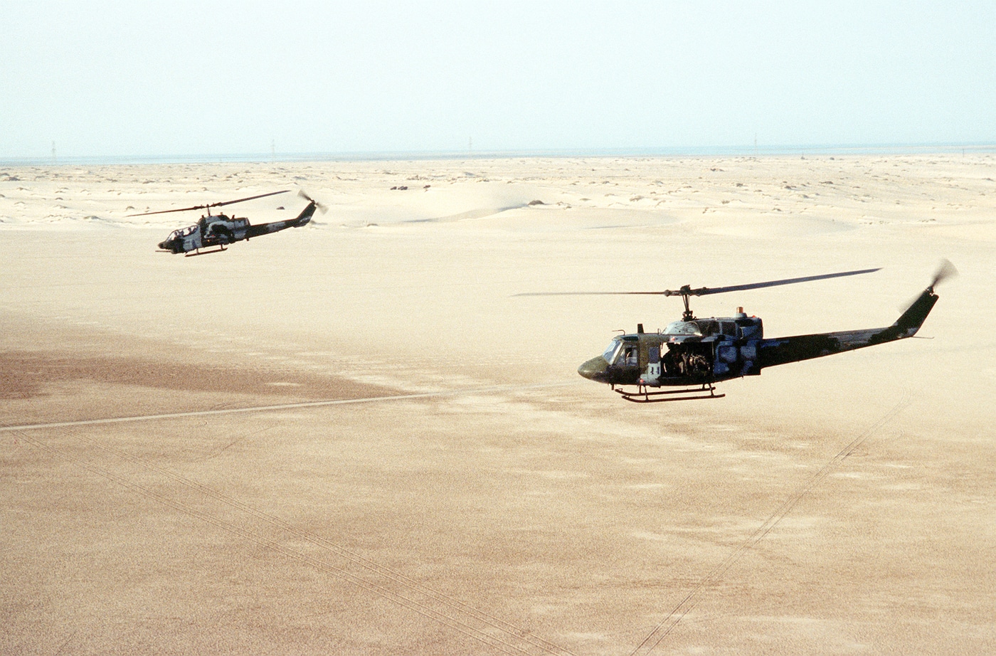 Shown in this photograph is a UH-1N Iroquois helicopter, foreground, and an AH-1 Sea Cobra helicopter fly over the desert in Saudi Arabia during Operation Desert Shield in 1991.