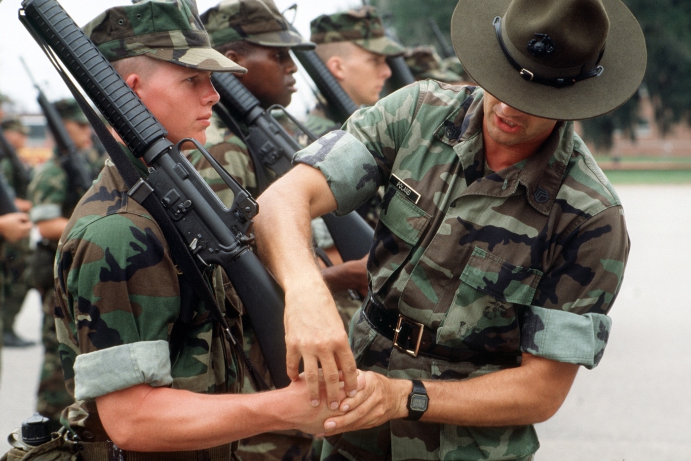 In this photograph, a USMC drill instructor teaches rifle drill to Marine recruits. The recruit Marines are carrying M16A2. The image is from the 	National Archives and Records Administration.