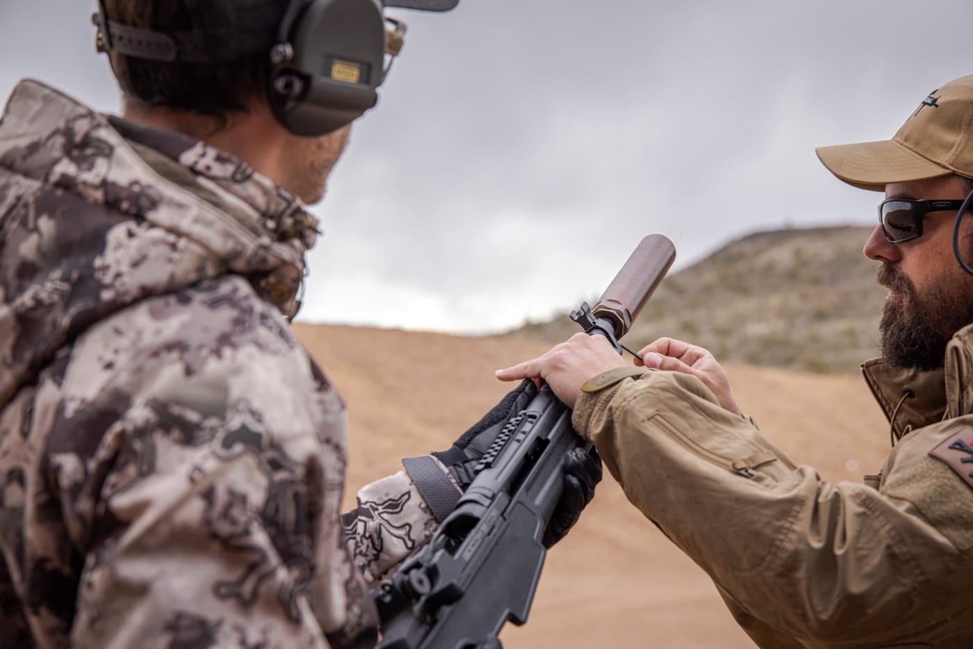 Photo of a shooter at an outdoor range firing a semi-auto rifle equipped with a suppressor. The suppressor extends beyond the handguard. The shooter wears ear protection, but the overall scene is quiet and controlled. The image illustrates real-world suppressor use, showing how it reduces noise and recoil during shooting.