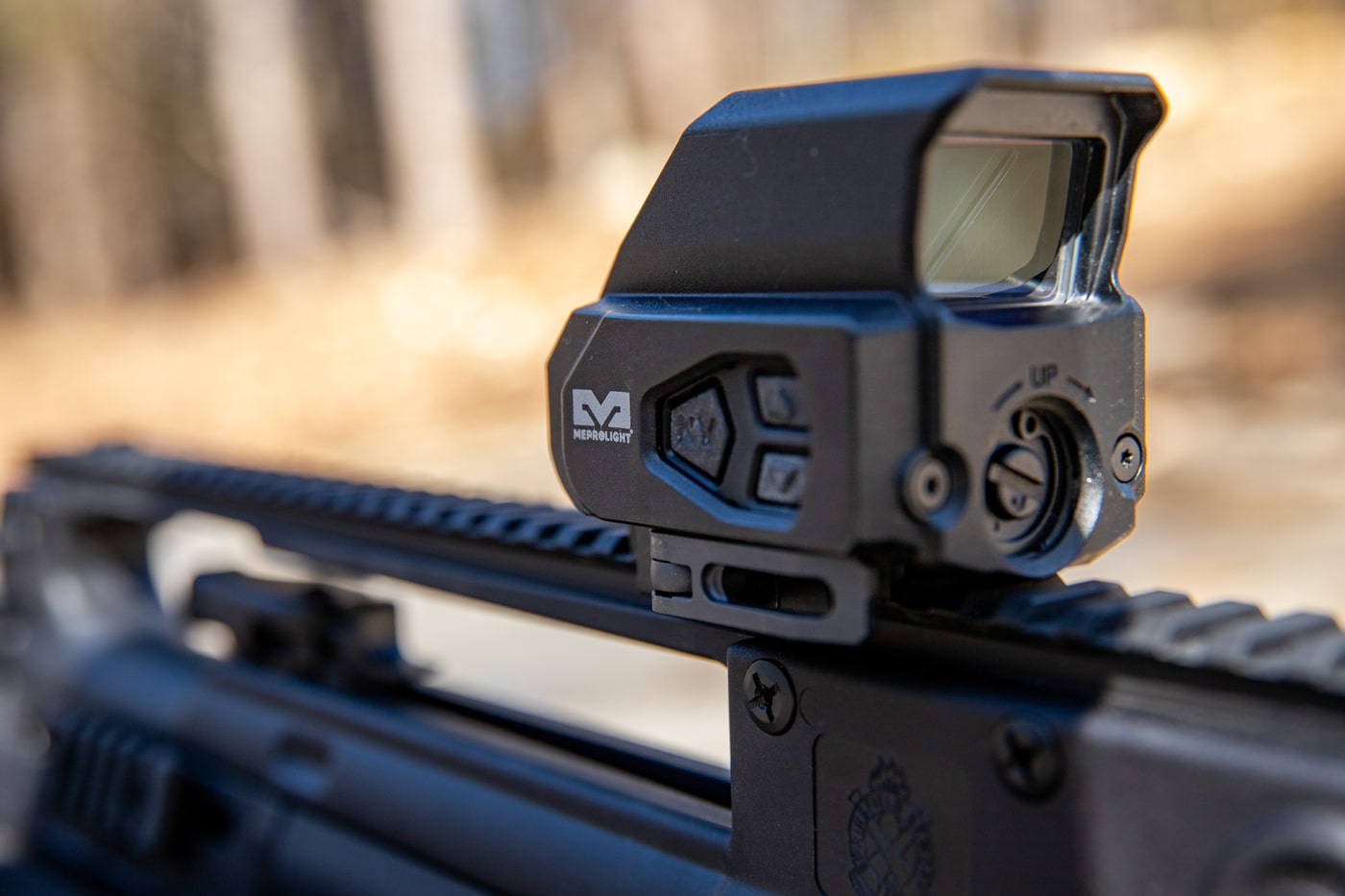Close-up of the Mepro Tru-Vision SR's control buttons on the left side. The buttons allow for manual brightness adjustment and reticle mode switching. The unit includes automatic brightness control with a light sensor on the top. The buttons are raised and tactile, designed for gloved use. Photo shows the control layout clearly with ambient lighting.