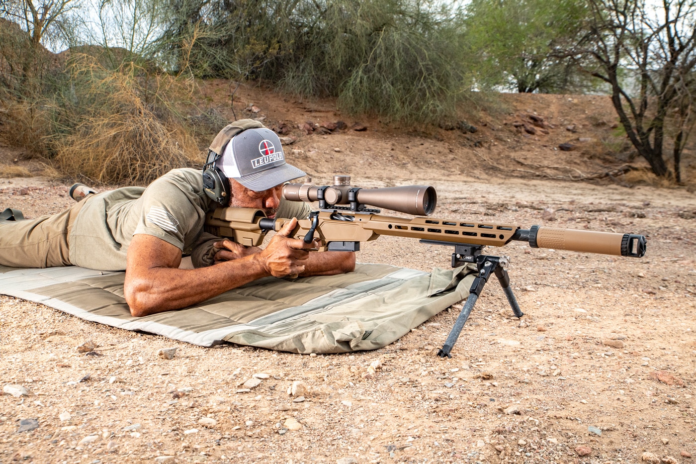 A Springfield Armory Model 2020 Heatseeker rifle is shown on a shooting bench with a scope and bipod attached. The rifle features a Sharps Bros. Heatseeker chassis, a lightweight carbon fiber-wrapped barrel, and a Coyote Brown Cerakote finish. A Leupold optic is mounted on the top rail, and a suppressor is attached to the muzzle. The bipod and bag support the rifle in a prone shooting position. This image highlights the rifle's configuration as tested in this Springfield Armory Model 2020 Heatseeker review.
