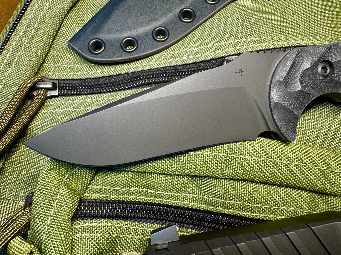 Side profile of the Mullet blade showing the drop point with a long, ground-in clip and slight belly recurve. The tip maintains a thick cross-section for strength while the recurve improves draw cuts. CPM M4 steel and Gunkote finish are clearly visible. The grind balances both slicing and piercing tasks. This is a practical design for field, defense, or utility use.