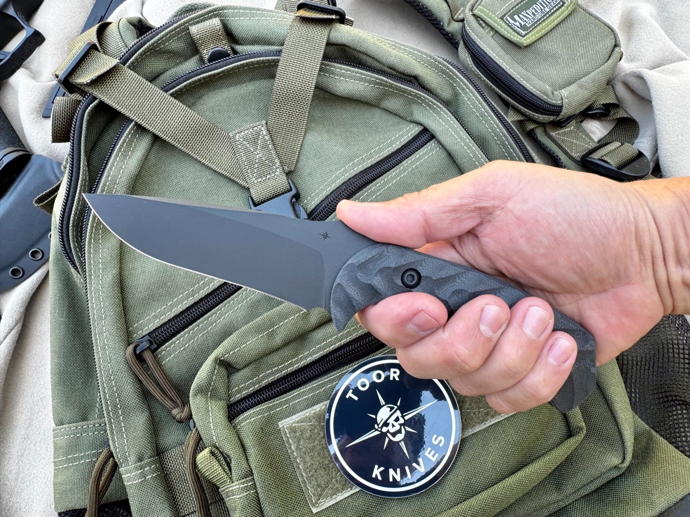 Close-up photo of the Mullet’s black G10 handle with pronounced dynamic fluting. The grooves are deep and angled to provide texture and grip during use. Gray liners add contrast between the handle and blade. This grip texture helps retain control in wet, muddy, or bloody conditions. Ideal for field use or emergency scenarios.