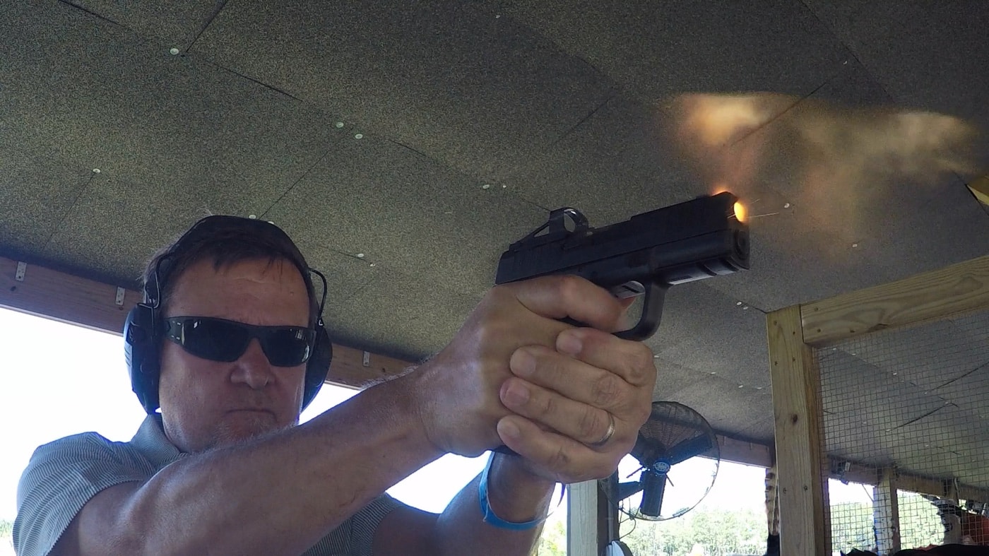 Still frame of a handgun being fired in low light with visible flash at both the muzzle and top port. The flash is bright but contained. The scene shows no disruption to the shooter’s vision or aiming ability. This image rebuts the myth that ported pistols cause blinding muzzle flash. Useful for illustrating flash patterns in defensive scenarios.