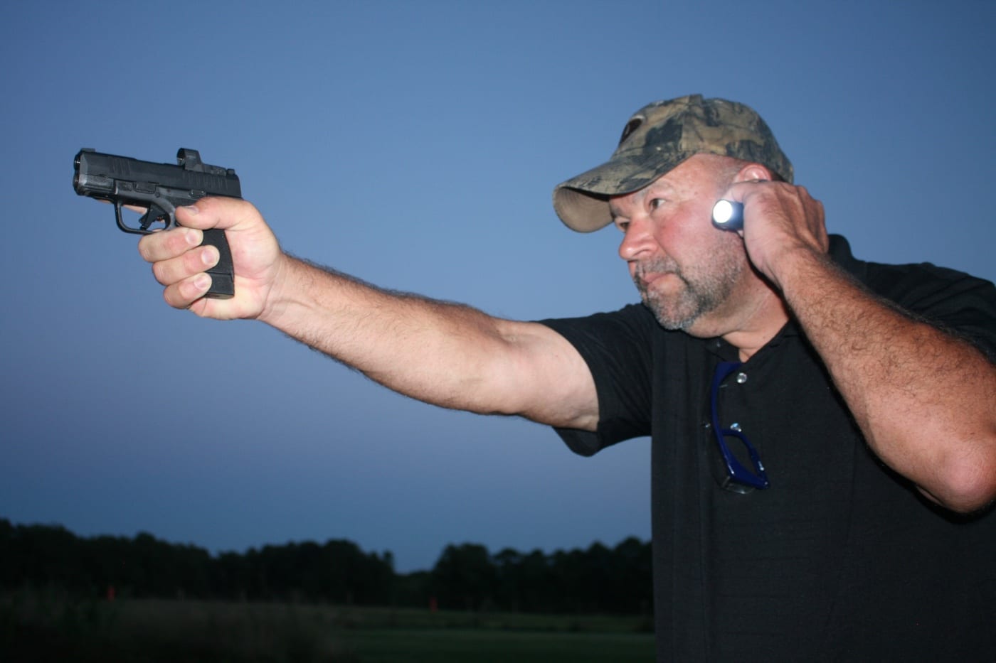 Image showing a shooter using the neck index flashlight technique with a handheld light and micro-compact pistol. The gun is pointed downrange, while the support-side hand holds the light near the jawline. The positioning allows illumination of the target zone without crossing the muzzle over unintended areas. This image supports the idea that handheld lights still have a place even if using a weapon-mounted light on micro pistols. Conflict avoidance and safe assessment remain critical priorities.