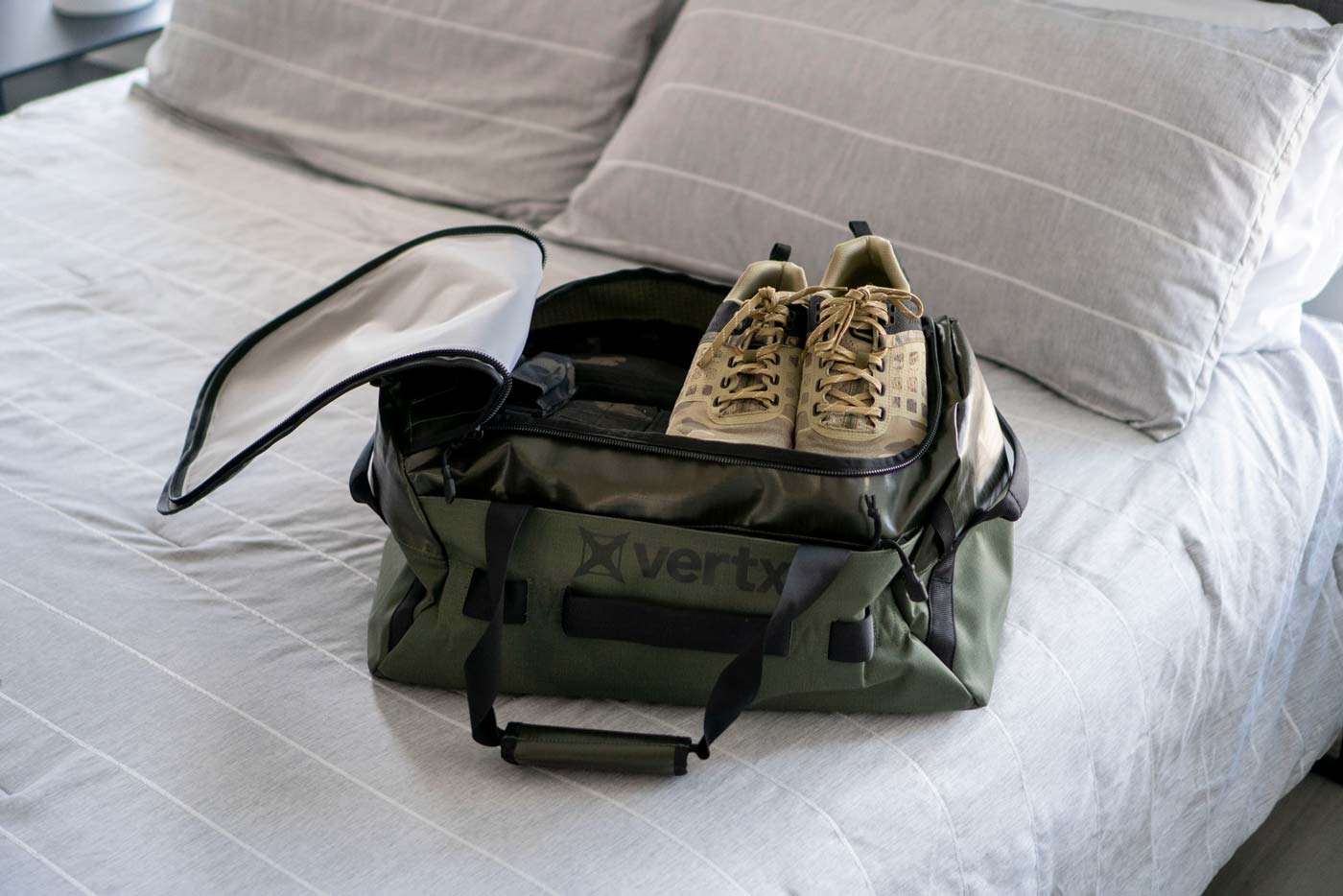 The Vertx RLT 50L Duffel Bag opened to show its contents packed with outdoor clothing and hiking shoes. The spacious interior of the tactical duffel demonstrates its practical capacity for adventure travel with clothing and gear neatly organized inside.