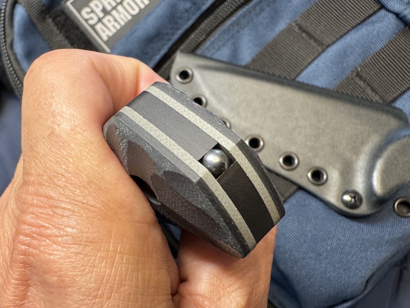 Close-up image of the tungsten carbide breacher ball embedded in the butt of the Toor Mullet’s handle. This hardened insert is used for breaking tempered or laminated glass in emergency situations. It's integrated directly into the full tang steel. This tool expands the knife’s use beyond just cutting. A useful feature for tactical, rescue, or vehicle-bound users.