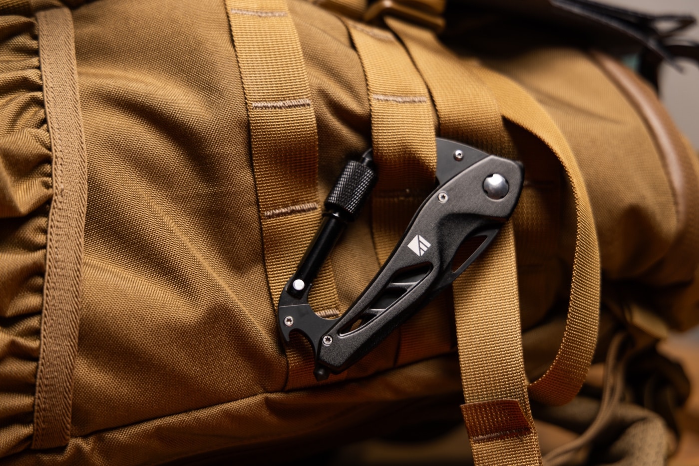Dark Energy review features the Carabiner Pro multi-tool attached to a pack’s gear loop using its built-in carabiner clip. The stainless steel construction and sharp locking blade are clearly visible alongside integrated screwdrivers and bottle opener. You can also spot the emergency window breaker tip at the end. It’s a compact 6-in-1 tool designed for rugged field utility in this Dark Energy review. The image communicates quick access to multipurpose outdoor tools.
