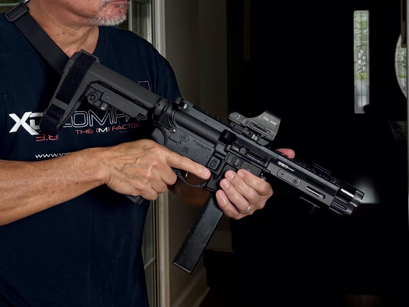 The photo shows the author holding a Springfield SAINT 9mm PCC (pistol-caliber carbine), which is positioned for defensive use inside a residential setting. This type of firearm is often selected for home defense because it provides maneuverability, adequate stopping power, and is easier to control in tight spaces like hallways and rooms. The image demonstrates awareness of firearm safety, with attention to muzzle direction and trigger discipline. Choosing an effective weapon is an important part of planning how to survive a home invasion, but it also requires knowledge of local laws and personal training. The author’s setup might include accessories like a sling or optic, which can further improve handling during a dynamic incident. Selecting reliable equipment is essential, but regular practice and familiarity with your firearm matter just as much for protecting yourself and your family in a crisis. This scenario highlights the gear and mindset often recommended for modern home security.