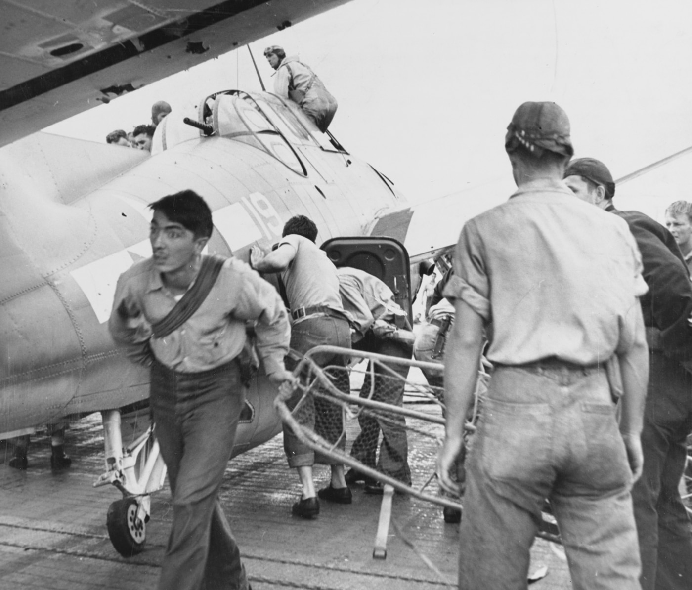 US Navy corpsmen help wounded airmen in a shot up TBF Avenger on USS Saratoga
