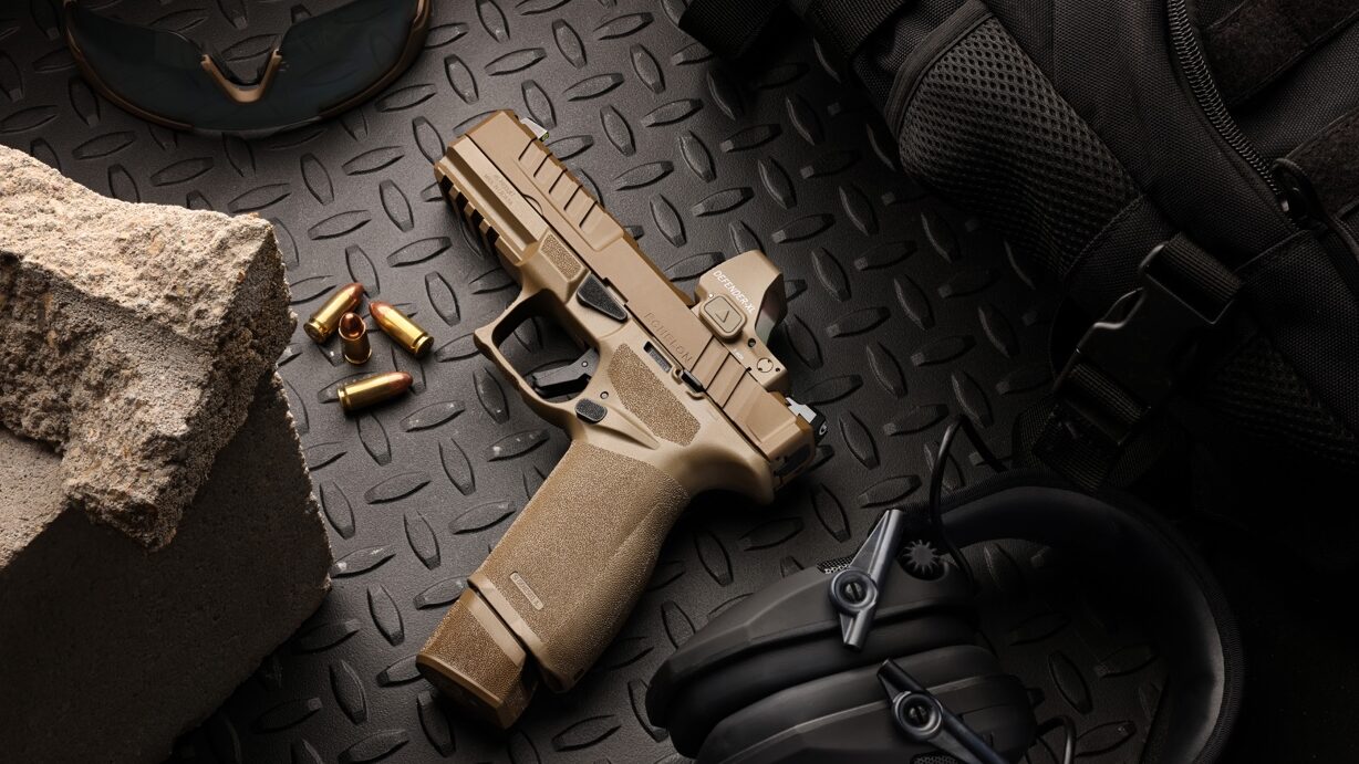 Side view of the tan Vortex Defender-XL red dot sight showing its full-size housing. The coyote brown finish is consistent across the body. The oversized aspherical viewing window dominates the frame. You can spot the Fast-Rack peaks above and below the lens. CR2032 battery cap and tool-less windage turret are visible.