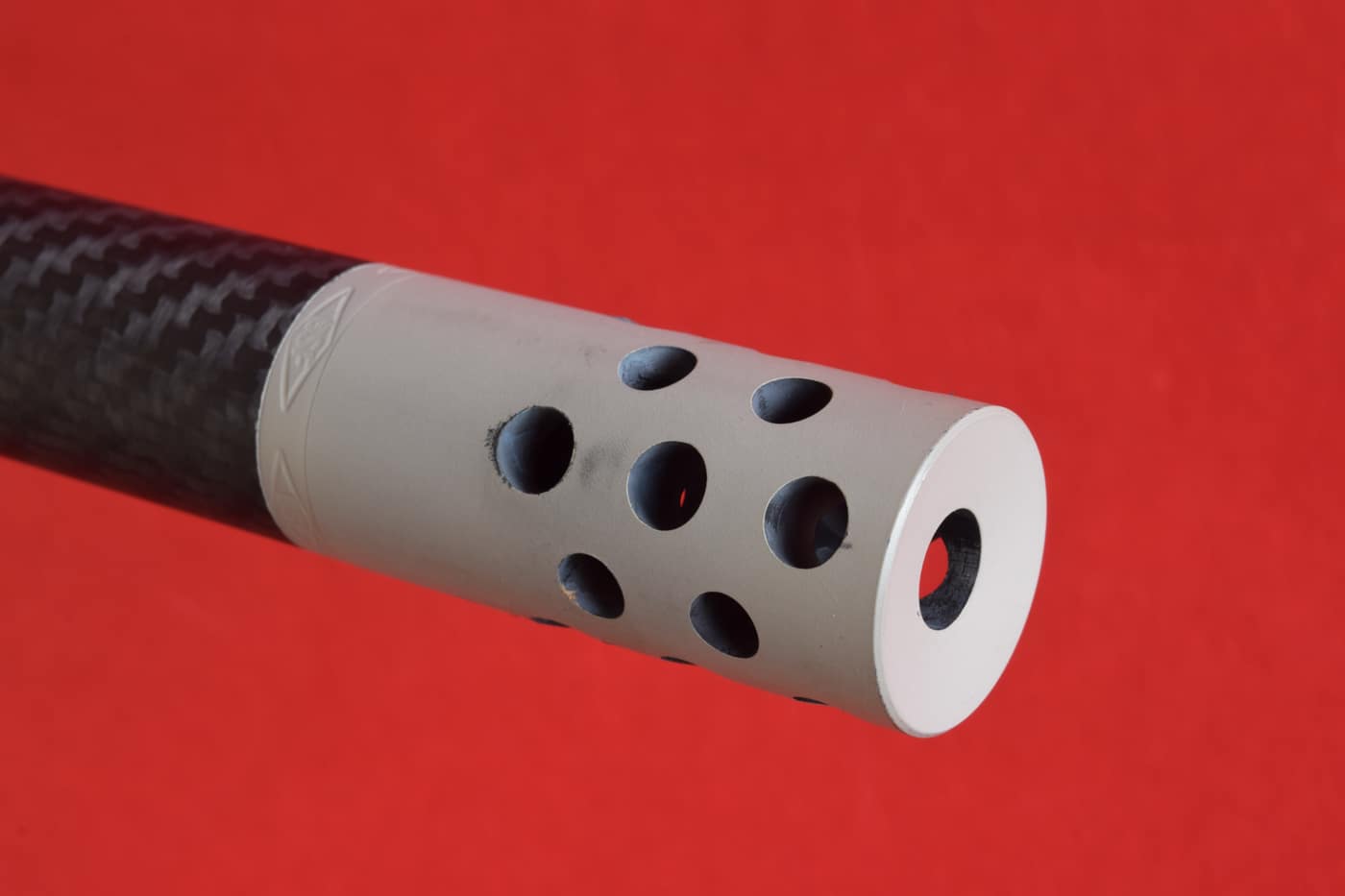 Close-up of a threaded muzzle brake attached to a .270 Winchester carbon-fiber barrel. The three-chamber brake ports are angled to direct gas and reduce recoil. A locking jam nut secures the device against unwanted rotation. The finish is Cerakoted, matching the barrel’s dark gray tone. This component hints at improved shootability and gentler recoil impulse. It underscores the balance between flat trajectory and shooter comfort.