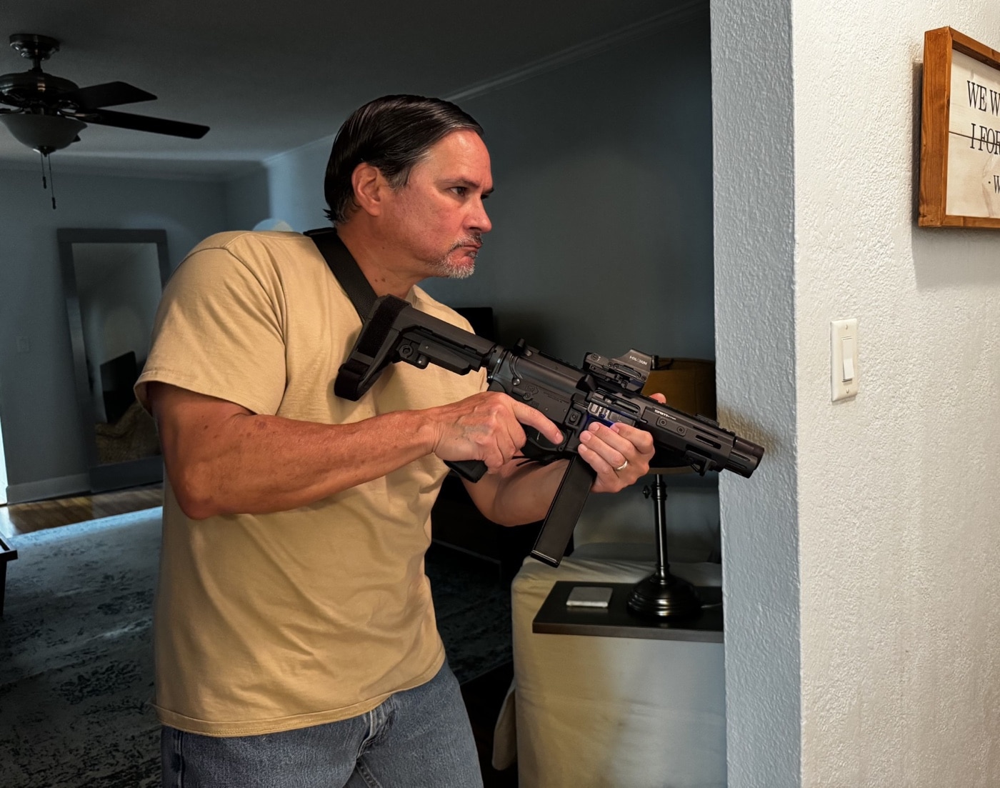 The author is pictured navigating through his house while holding a Springfield Armory SAINT PCC 9mm, demonstrating methods for clearing rooms and hallways during a simulated home invasion event. He maintains a ready but controlled posture, using proper firearm handling and keeping the muzzle downrange. This situation highlights the need to move deliberately and stay aware of your surroundings, especially if you believe an intruder may be present or hiding inside your home. The photo serves as an example of tactical movement, showing how to combine home defense equipment with practical skills for survival. Successfully surviving a home invasion often comes down to preparation, training, and knowing how to respond under stress. Familiarity with your environment, your firearm, and family safety protocols all play a role in your response. Staying cautious and methodical greatly improves your odds in a residential break-in.