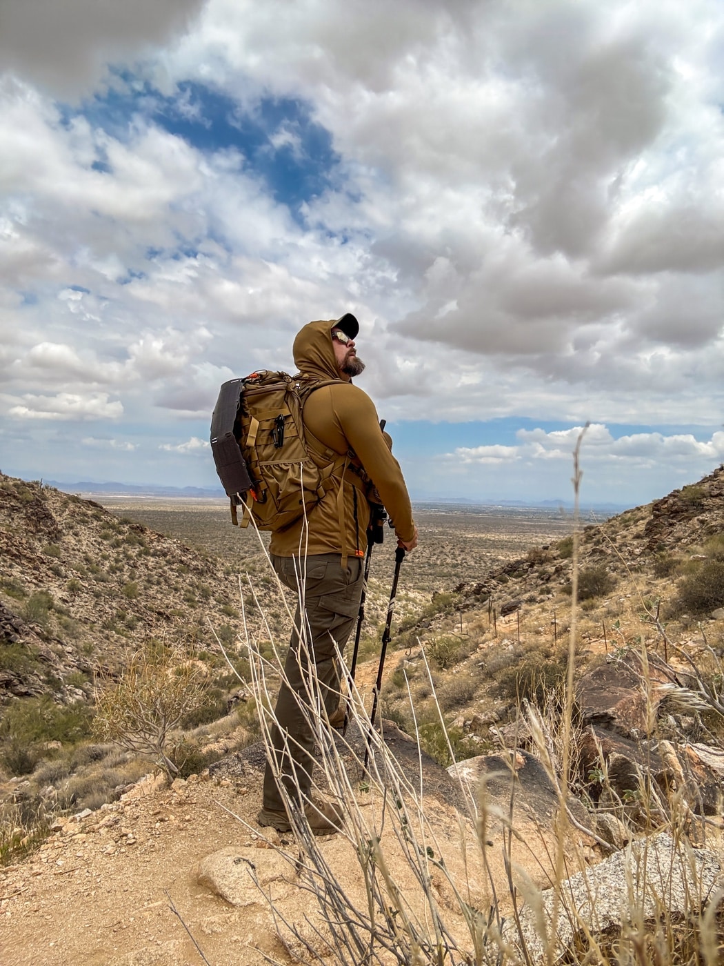 Dark Energy review photo captures the author hiking a desert ridgeline with the Spectre solar panel secured to his backpack. The collapsible charger unfolds mid-stride and tilts toward peak sun exposure. Weathered sandstone formations fill the background, highlighting harsh conditions. The braided paracord cable snakes into the pack, hinting at steady off-grid charging. This image highlights dynamic solar harvesting during motion and the practicality of portable power gear. It demonstrates field-ready energy generation in remote terrain.