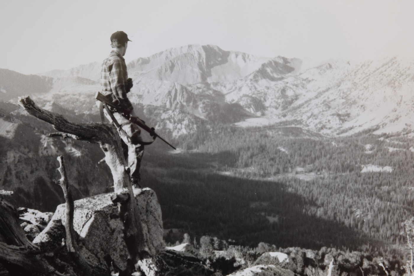 A lone hunter stands on a rocky ridge overlooking the rolling peaks of Oregon’s Wallowa Mountains at dusk, a bolt-action rifle chambered in .270 Winchester slung across his back. The carbon-fiber stock and fluted barrel catch the fading light as he pauses to scan the valley for game. Early-season elk country. A crisp breeze ruffles his camo jacket and hat brim, suggesting thin air and cold mornings. His stance hints at field readiness and the flat trajectory offered by the .270 Winchester’s high muzzle velocity. The distant ridgelines and deep coulees fade into blue shadows, emphasizing the long-range potential of the cartridge. The mild recoil reputation of the .270 Winchester allows for steady follow-up shots during mountain hunts. A spotting scope rests on his pack, underscoring the cartridge’s consistent downrange energy past 300 yards.