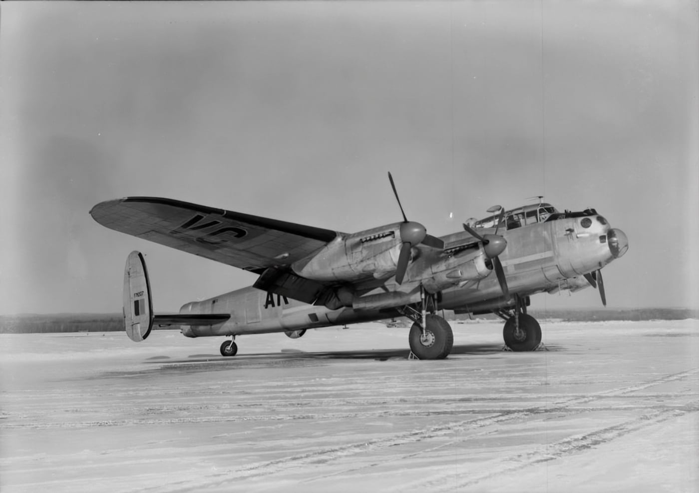 The image shows Canadian Avro Lancaster FM207 parked on a runway, photographed from the side or at a slight angle. The bomber’s four-engine layout, twin tailfins, and expansive wingspan are all visible, along with Royal Canadian Air Force markings on the fuselage and wings. The aircraft is stationary, with its wheels on the tarmac and the propellers at rest. Surrounding the Lancaster is an open airfield environment, possibly including grass, taxiways, or distant airport infrastructure. FM207’s paint and insignia are well maintained, emphasizing the importance of preservation and commemoration in Canada. The scene is peaceful, with no crew present or boarding activity, underlining that the aircraft is now retired and on static display. The photograph is ideal for illustrating articles on Canadian aviation history, postwar use of the Lancaster, or the role of the RCAF in WWII and beyond.
