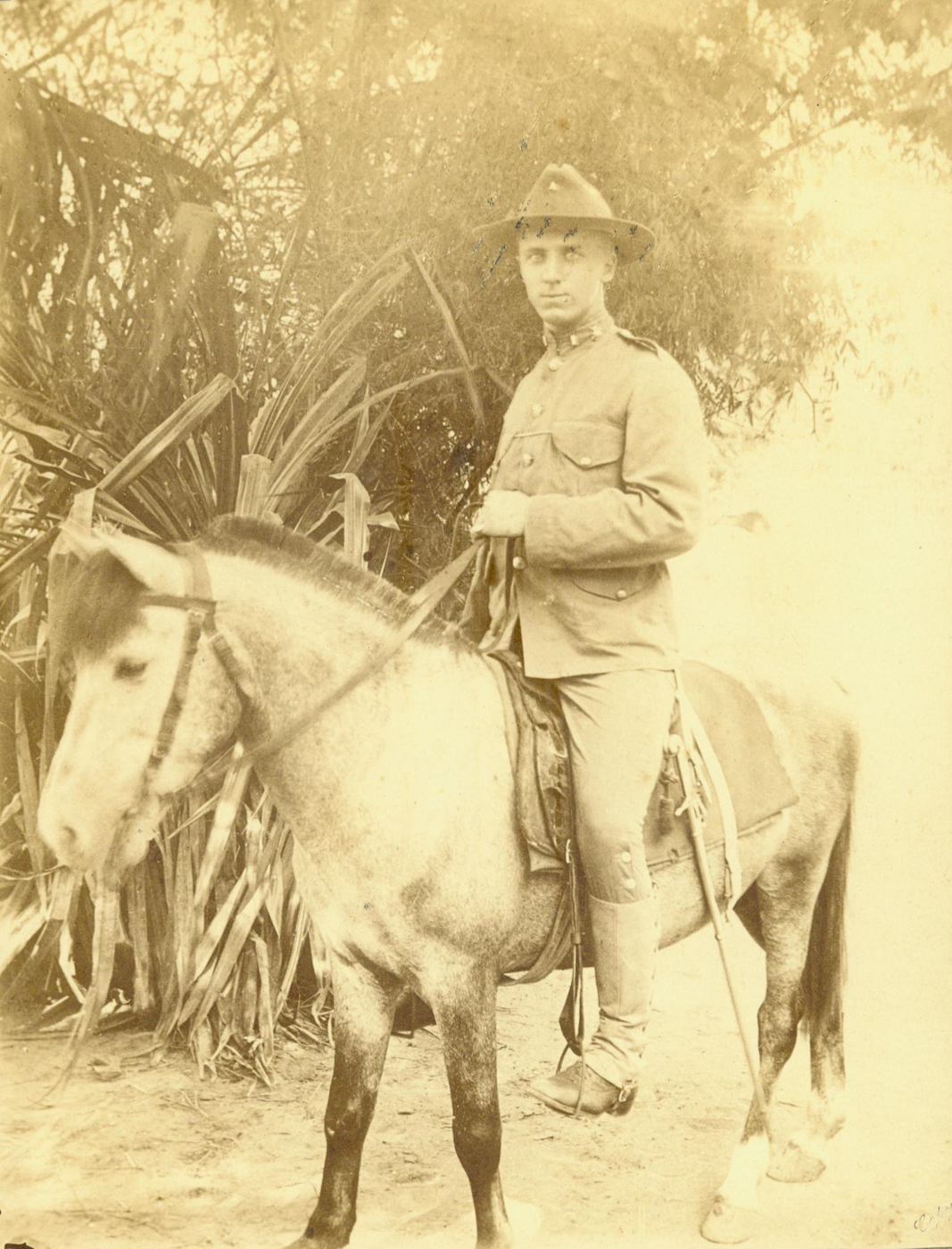 Captain Smedley Butler, dressed in U.S. Marine Corps officer’s uniform circa 1901, sits confidently atop a sturdy horse in China during the aftermath of the Boxer Rebellion. Butler’s attire includes a campaign hat, riding boots, and a visible sidearm, marking his status as a Marine officer on active duty. The horse is outfitted with a simple saddle and bridle, and both rider and animal appear alert and ready. The background may feature a dusty road, scattered buildings, or hints of the Chinese countryside and local architecture. Butler’s posture is upright and commanding, reflecting both his youth and growing reputation for battlefield leadership. This image illustrates the reality of American military presence in China after the rebellion and captures a moment in the career of a future two-time Medal of Honor recipient. The scene provides context for the challenges faced by Marines in foreign environments at the start of the 20th century.