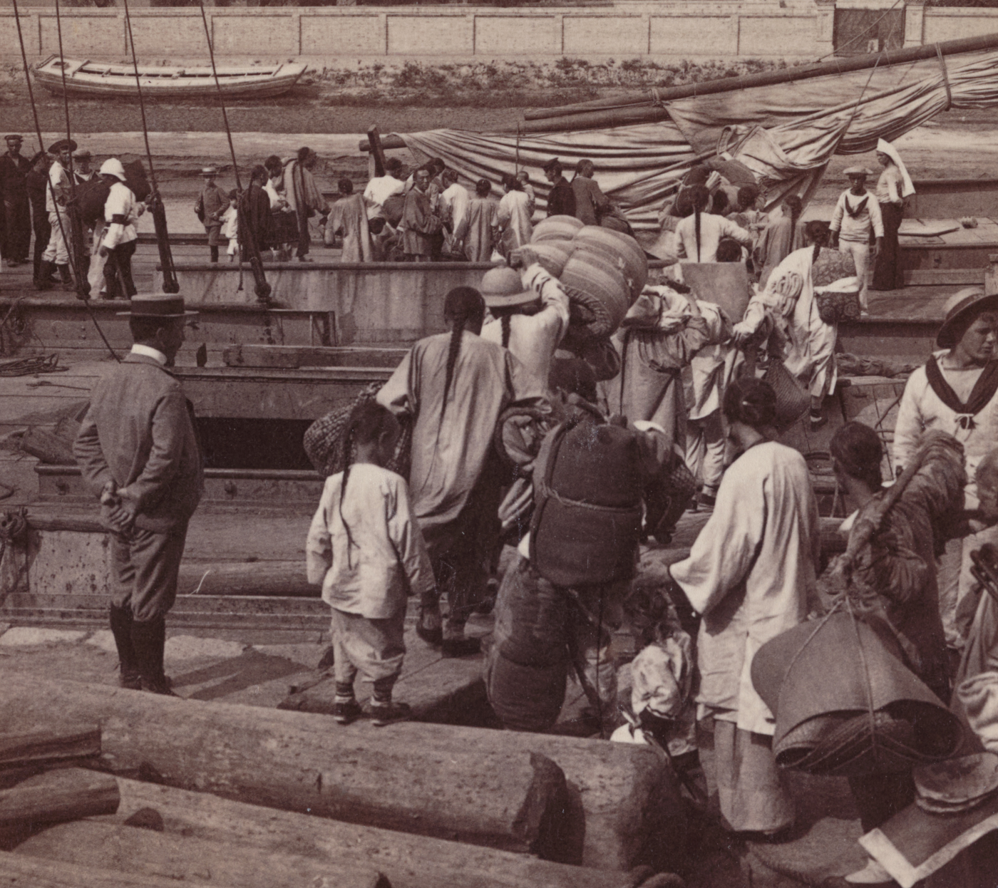 A group of Chinese Christian refugees, including men, women, and children, is shown hastily boarding small wooden boats at a riverbank or port, fleeing violence during the Boxer Rebellion. Some are carrying bundles of personal belongings, while others help elderly relatives or young children onto the crowded boats. Their clothing is simple and practical, indicating they left home in a hurry, and their faces show fear, exhaustion, and uncertainty about their future. In the background, there may be other groups waiting to board, stacks of luggage, and possibly local boatsmen helping push off from the shore. The scene illustrates the desperation of Chinese Christians forced to abandon their homes due to targeted attacks by Boxer rebels. The refugee movement put significant strain on surrounding regions and drew urgent responses from foreign missionaries and aid organizations. This photo captures the scale of displacement and the vulnerability of religious minorities during the 1900 uprising.