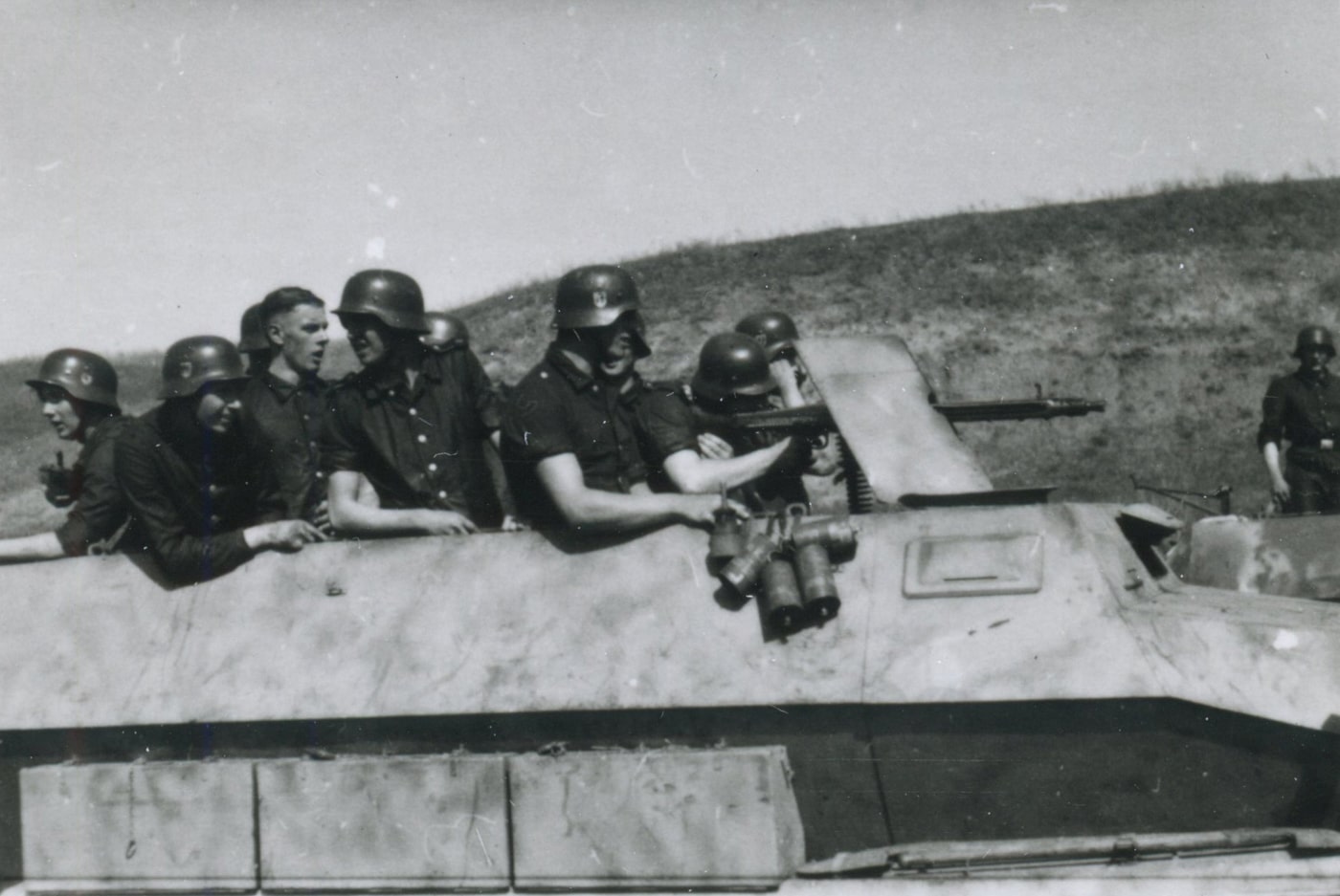 World War II photo from captured SS war correspondent archives, showing German SS troops operating a vehicle-mounted MG 42 on an Sd.Kfz. 251 halftrack on the Eastern Front. One soldier fires the MG 42 from a fixed mount, while others stand by for support or to observe the results. The halftrack’s design and details — such as armor plating and open rear compartment — are visible. The environment looks harsh and muddy, matching common Eastern Front combat settings. This image demonstrates the integration of the MG 42 machine gun with armored vehicles for increased firepower.