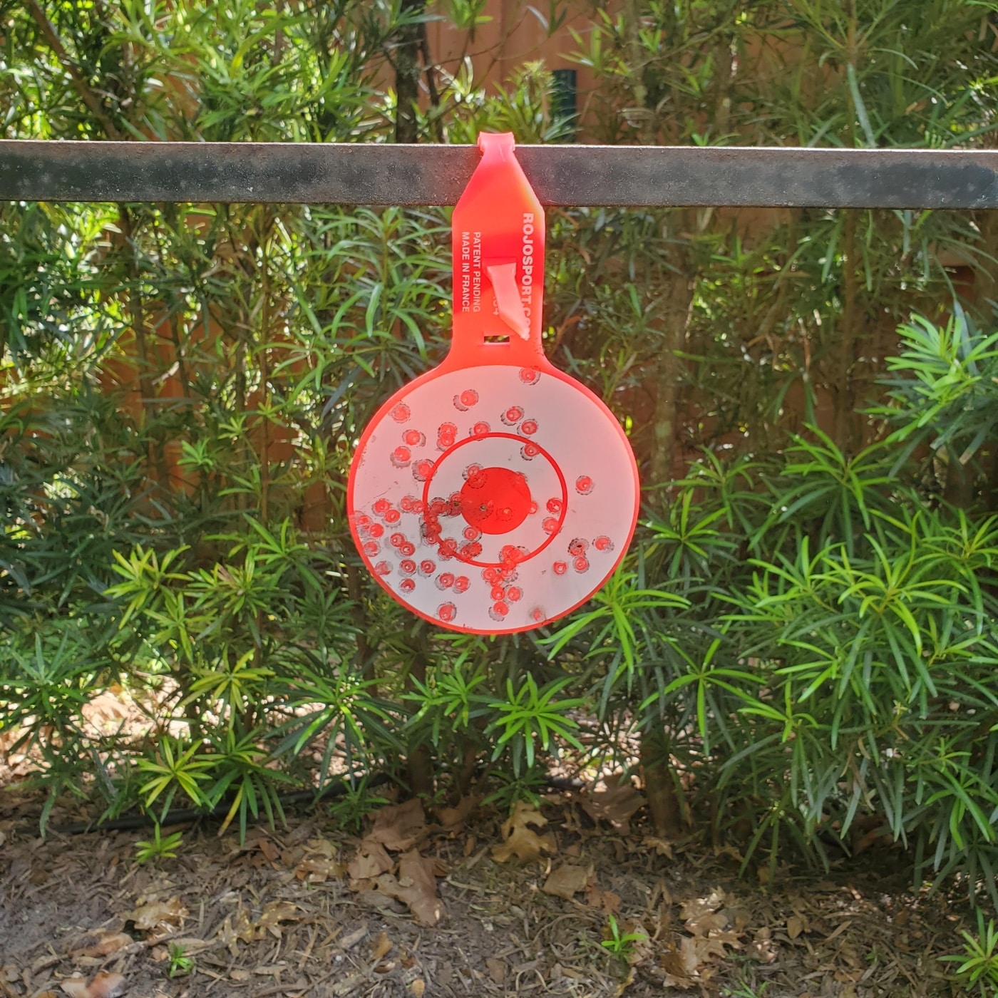 A ROJO RJ4 Tactical Target is shown up close with many visible pellet marks and holes across its surface. The red bullseye and white printed rings are still clearly visible despite heavy use. You can see concentrated shot patterns, including some overlapping impacts where the target took repeated hits. The polyurethane material shows surface wear but holds its shape, with no major cracks or broken pieces. This photo is a practical example for the Rojo RJ4 Tactical Target review, highlighting real-world durability after extensive range sessions.