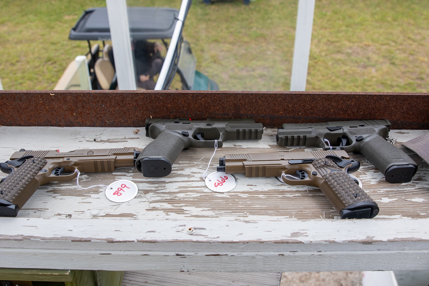 The photo shows a display of Springfield Armory prize guns arranged on a table at the Shootoff event. Prominently featured are several TRP 1911 pistols, each with classic styling, robust frames, and checkered grips, known for their accuracy and reliability in competitive shooting. Next to them are Springfield Armory Echelon pistols, recognizable for their modern polymer frames, optics-ready slides, and modular features. The pistols are laid out neatly, each positioned for clear viewing, with event signage or branded mats possibly visible underneath. The lighting highlights the craftsmanship and distinguishing details of both pistol models. These firearms are presented as prizes for the event’s top competitors. The image underscores the prestige of the awards and Springfield Armory’s commitment to supporting shooting sports.