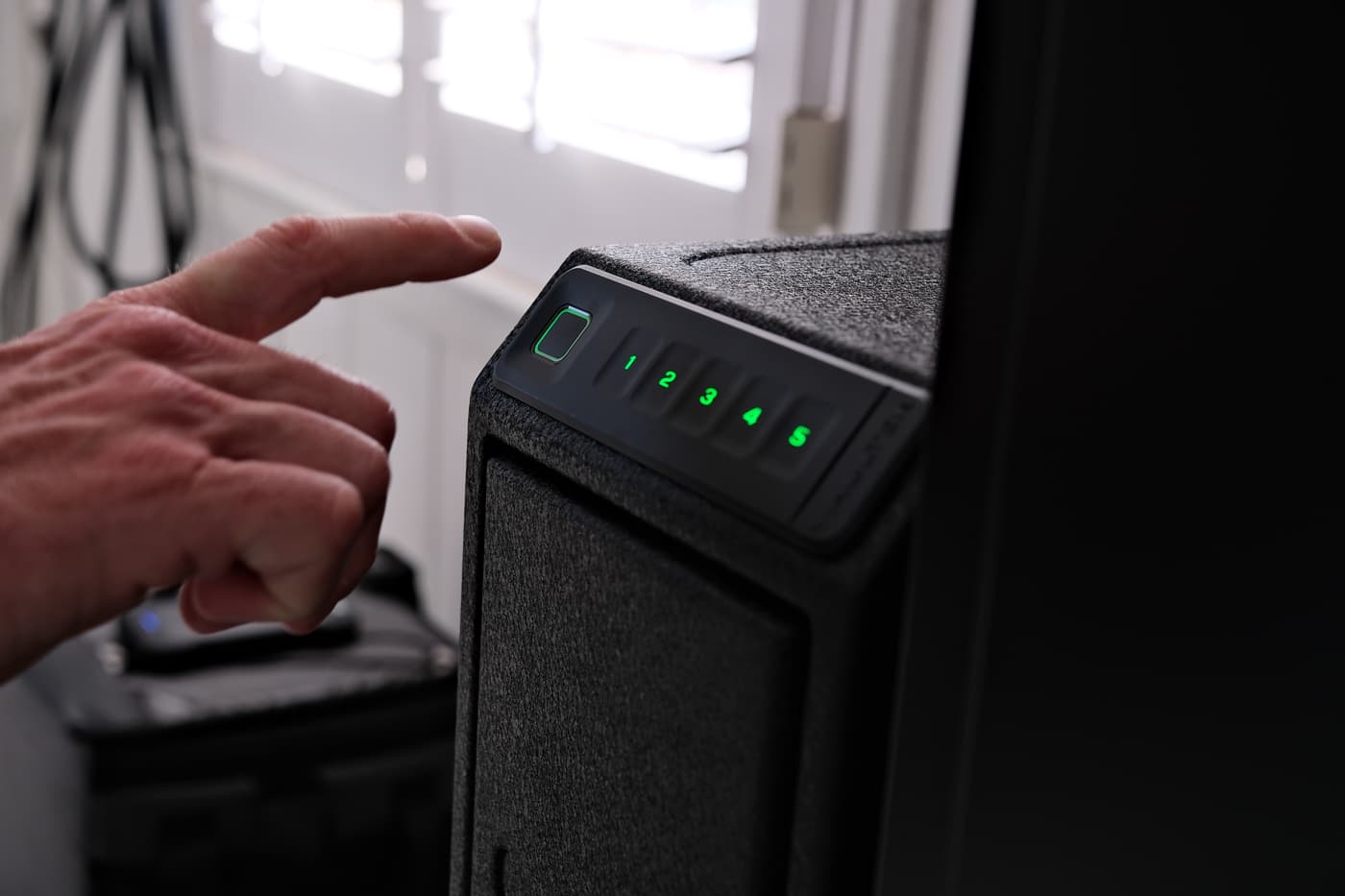 A man’s hand is shown pressing numbers on the electronic keypad of a Vaultek RS Slider Safe in this photo. The keypad is illuminated and clearly labeled, making access simple even in low light. The safe itself has a slim, steel housing and its drawer is closed, about to be opened by the entered code. You can also see the fingerprint scanner next to the keypad, showing that multiple unlocking methods are available. This setup illustrates how the RS Slider offers fast entry for authorized users, combining security with convenience. The moment captured demonstrates real-world, practical use by an owner seeking immediate firearm access. This ALT text is suitable for those researching quick-access gun safes and looking for electronic lock operation visuals.