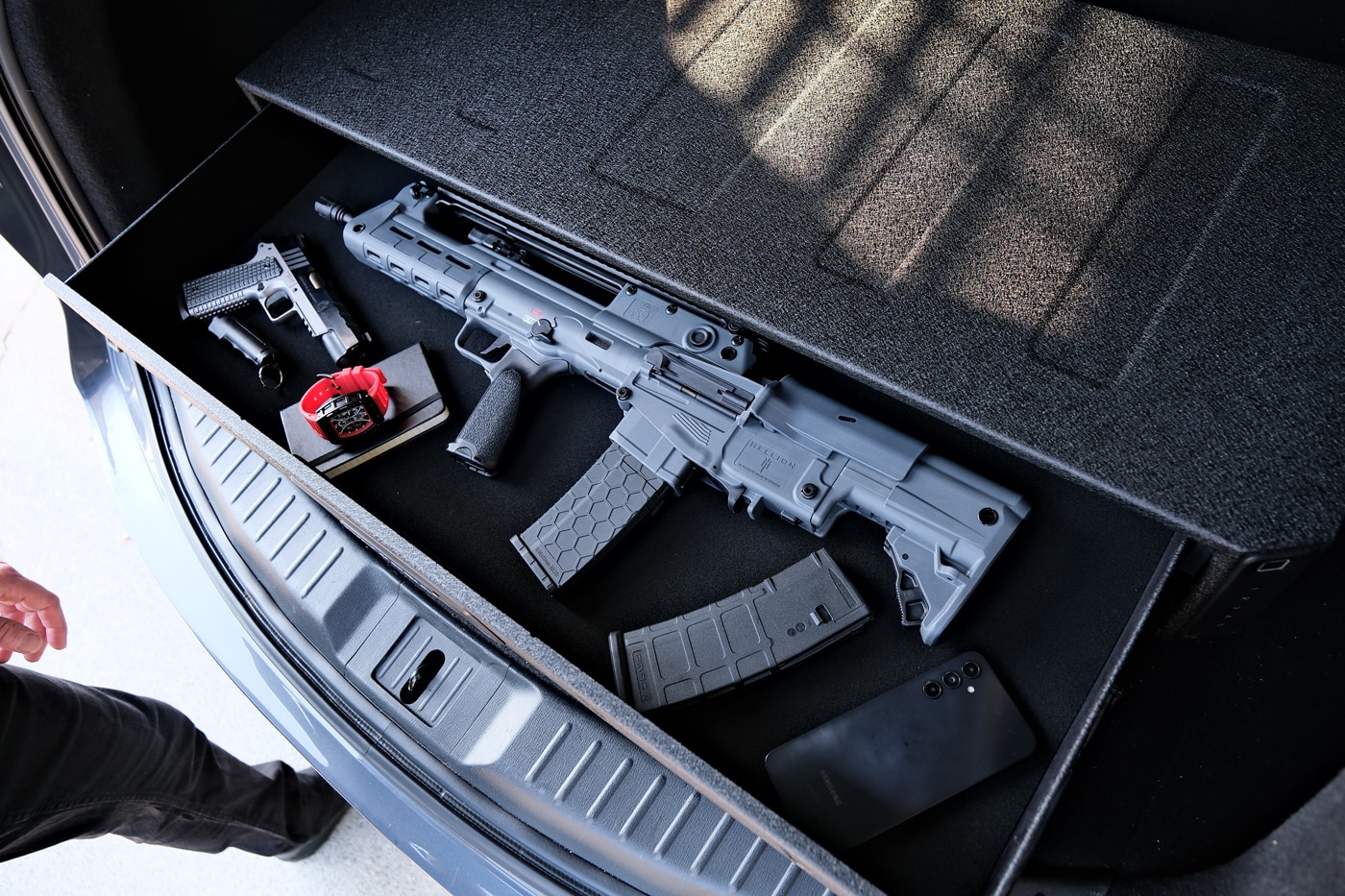 This image shows the Vaultek RS Slider Safe mounted in the cargo area of an SUV, with its drawer fully extended and containing a Springfield Armory Hellion rifle. The drawer’s internal LED lighting clearly illuminates the rifle, making the firearm and accessories easy to see and access. The safe fits neatly within the rear compartment and is secured in place, demonstrating how the RS Slider can be used for secure rifle transport in a vehicle. The spacious drawer provides a stable area for the rifle, along with room for additional gear or magazines. The vehicle interior is visible around the safe, confirming the automotive context. The Springfield Hellion’s bullpup design emphasizes the safe’s compatibility with a variety of tactical firearms. This photo is ideal for readers comparing vehicle gun safes and seeking secure ways to store AR-style rifles while traveling.