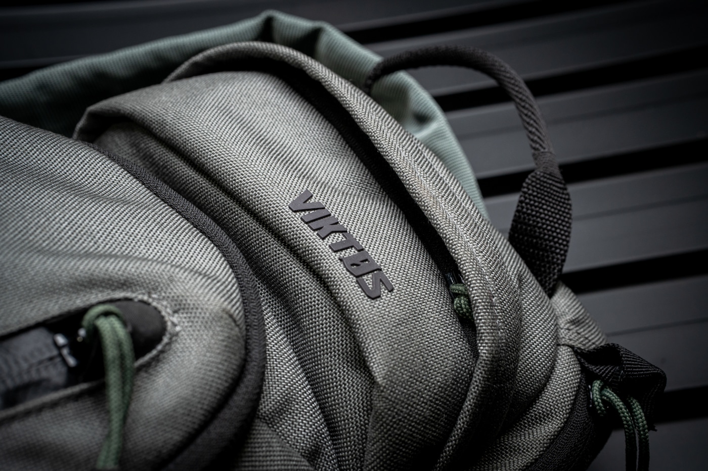 Close-up photograph showing the Viktos logo stitched onto the exterior of the Upscale 3 Slingbag, alongside a section of reinforced stitching and a heavy-duty zipper. The image focuses tightly on the bag’s branding and craftsmanship, with detailed views of the fabric texture, thread work, and zipper teeth. This shot demonstrates the overall build quality that Viktos is known for, emphasizing durability and attention to detail. The lighting clearly brings out the stitching pattern and the precise logo embroidery. This image is used in the Viktos Upscale 3 Slingbag review to show readers the quality materials and construction up close. The background is blurred to keep focus on the bag. Designed to help users understand the ruggedness and longevity of this concealed carry sling bag.