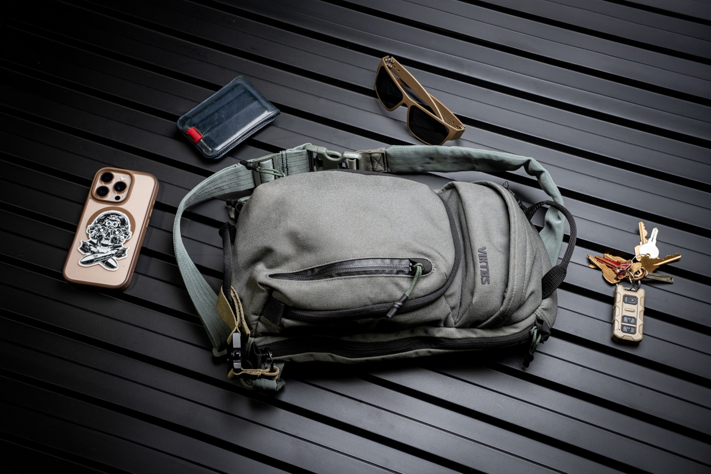 Detailed image of the inside of the Viktos Upscale 3 Slingbag, filled with common EDC gear: keys, a mobile phone, pocket knife, pen, and a compact flashlight. Each item is shown placed in its own section or pocket, demonstrating the bag’s design for keeping items separated and easy to find. The phone is placed in a protected pouch, while the keys are attached to a built-in key clip. The bag’s zippers and interior lining are visible, supporting the review’s focus on organization and ease of use. The Viktos logo is partially visible in the shot, reinforcing brand identity. This is a helpful visual for anyone curious about how much gear the Upscale 3 can handle for day-to-day needs. The focus is on clarity and functionality.