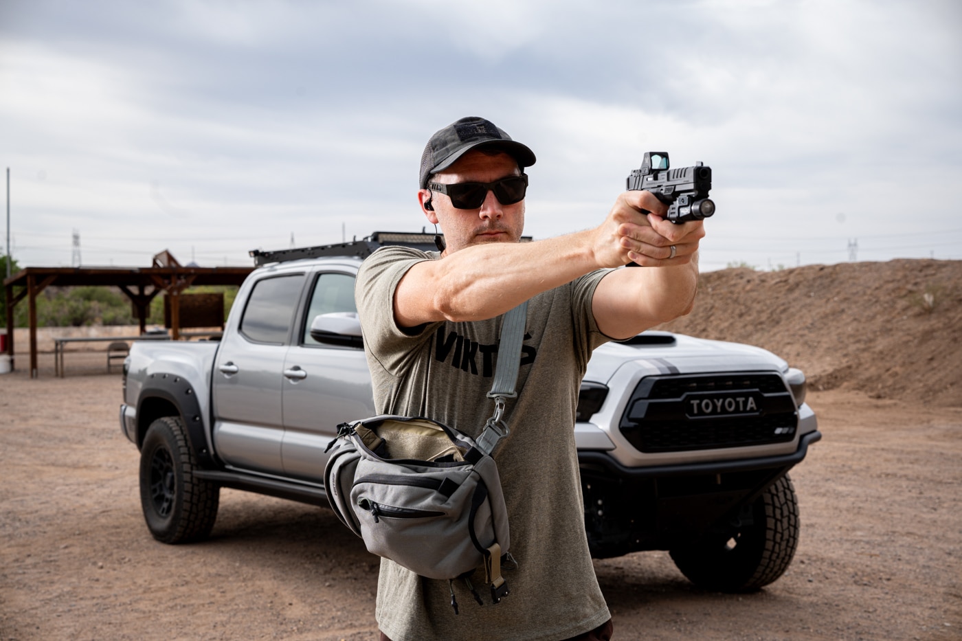 Photo of the author standing at an outdoor shooting range, firing a Springfield Armory Echelon pistol at a visible target downrange. The pistol was drawn from a Viktos Upscale 3 Slingbag, which is seen slung across the author’s body or placed on a nearby bench. The author is wearing range-appropriate clothing, eye protection, and hearing protection. Spent casings may be visible in the air, and the author is focused on their shooting stance, demonstrating controlled fire and proper grip. The background includes standard range elements like shooting lanes, berms, and steel or paper targets. This image is used in the review to show the process of drawing from the sling bag and transitioning smoothly to live fire practice. The scene emphasizes both preparedness and the importance of realistic training.