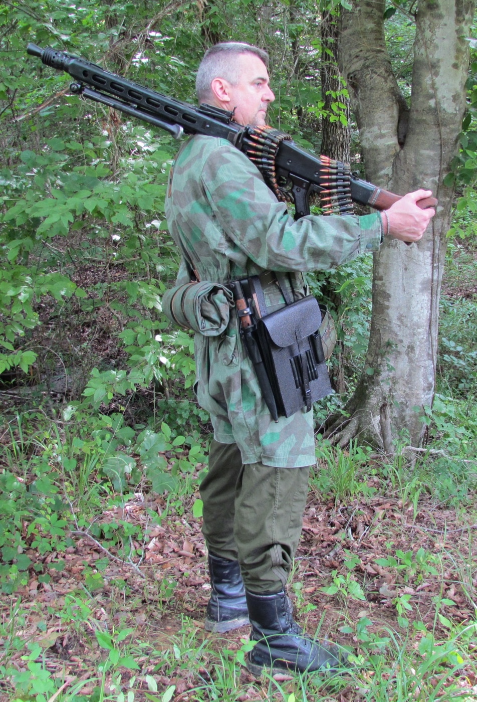 The author stands holding an MG 42 machine gun, showing the full length of the weapon from buttstock to barrel. He is dressed in modern casual clothing, contrasting with the historic World War II-era machine gun. The MG 42’s bipod is visible, and the author’s grip highlights the weight and size of the gun. The background is neutral, with no distracting elements, keeping the focus on the author and the MG 42. This image gives a sense of the MG 42’s scale when handled by an individual and provides context for the article about the weapon’s history.