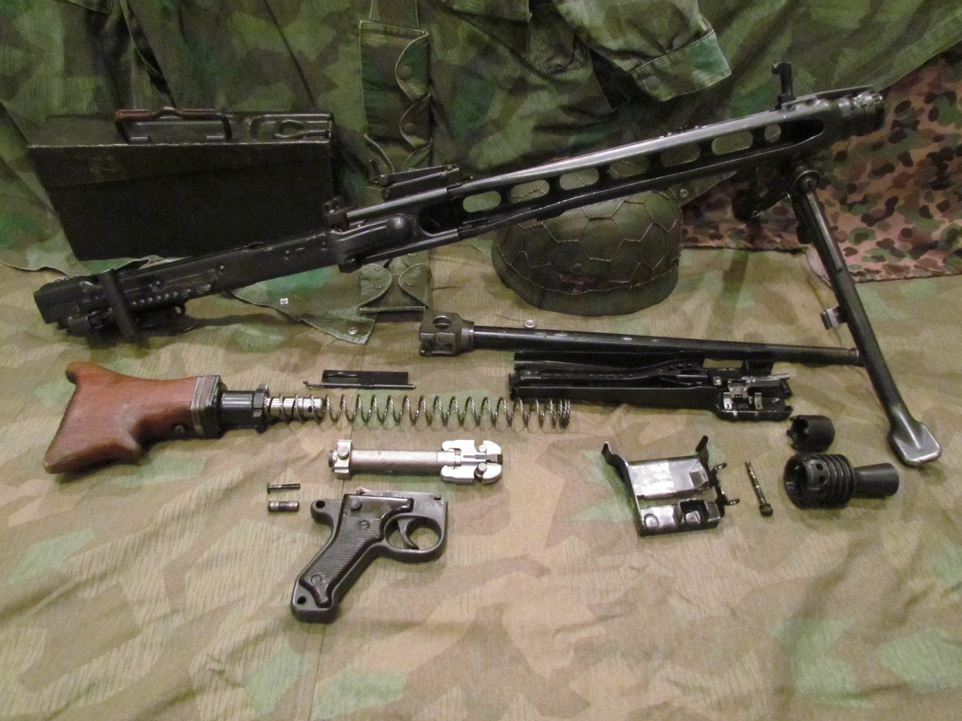 The MG 42 machine gun is shown in a field stripped state, with major assemblies like the barrel, bolt, recoil spring, and bipod removed from the main receiver. The components are spread out to display the internal layout and ease of disassembly. This view helps illustrate how quickly an MG 42 could be taken apart for cleaning or repairs during World War II. The image is well-lit and clear, making each part of the MG 42 machine gun easy to recognize for reference or instruction.