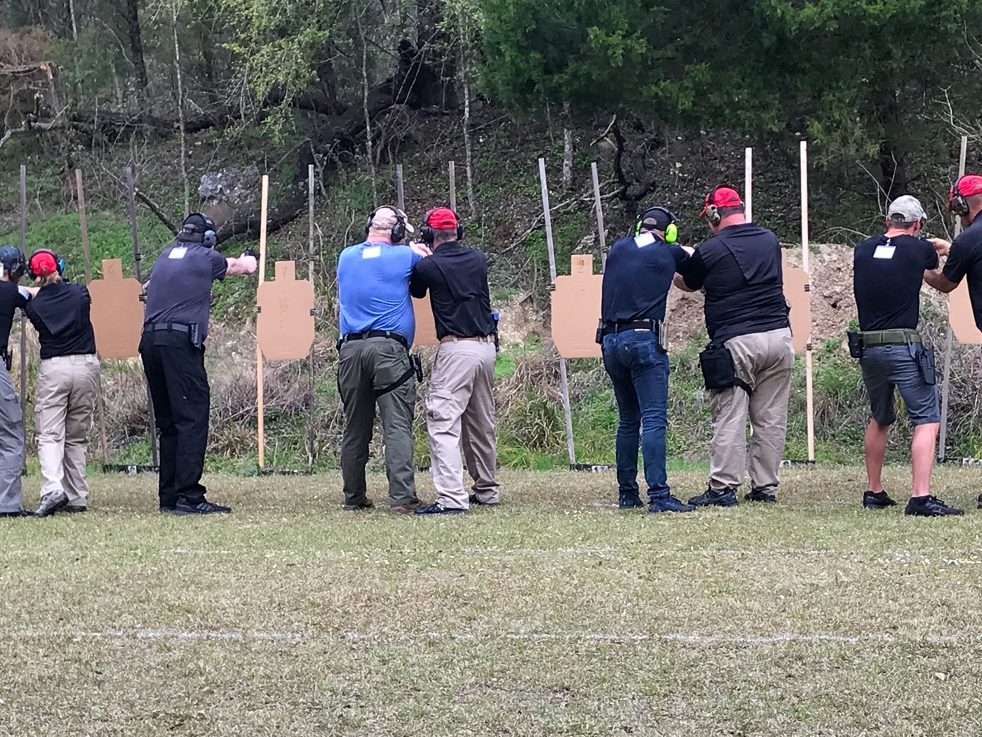 The photo shows firearms instructors from the Massad Ayoob Group standing alongside students on an outdoor shooting range. The trainers provide close guidance as students practice defensive shooting techniques, focusing on safe gun handling and correct form. Ear and eye protection are worn by all participants, highlighting the emphasis on safety during live-fire drills. The trainers appear attentive and engaged, giving direct feedback and instruction. This scene illustrates the value of professional firearms training, which can later serve as documented evidence in a self-defense trial to demonstrate responsible preparation.
