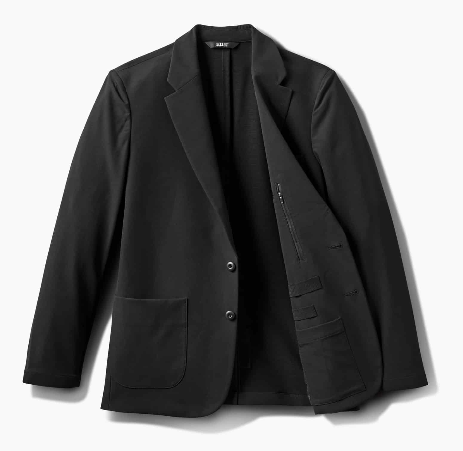 This photo shows the 5.11 Founder’s Jacket fully open, focusing on the inside where a prominent zippered pocket is visible on the chest. Other features, like elastic retention loops, dump pockets, and specialized compartments, are clearly displayed. The layout makes it easy to organize everything from a phone to a small walkie-talkie or extra magazine, while keeping items secure and discreet. The material looks strong but flexible, with reinforced stitching and a sleek, low-profile lining. This image is meant to give readers a close look at the tactical utility hidden inside the Founder’s Jacket. It highlights how the jacket is designed for both everyday carry and professional security work.