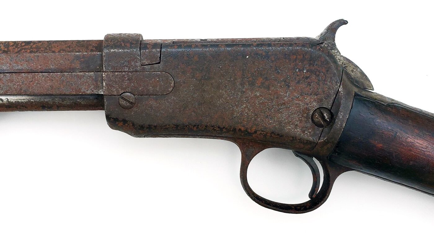 A close-up image of a pump-action .22 rifle receiver with obvious surface rust covering part of the metal. The rust appears as orange and brown discoloration along the side of the receiver, showing the effects of moisture and neglect. The rest of the rifle, including the wooden stock, is partly visible in the background but out of focus. This photo illustrates the kind of rust damage that can happen if a firearm is stored improperly or not maintained. The main purpose of this image is to show readers that rust can be removed from a gun using common techniques and tools. Taking action quickly can stop further corrosion and preserve the rifle’s function and appearance. The photo supports the primary keyword, “how to remove rust from a gun,” and demonstrates what surface rust looks like before cleaning.
