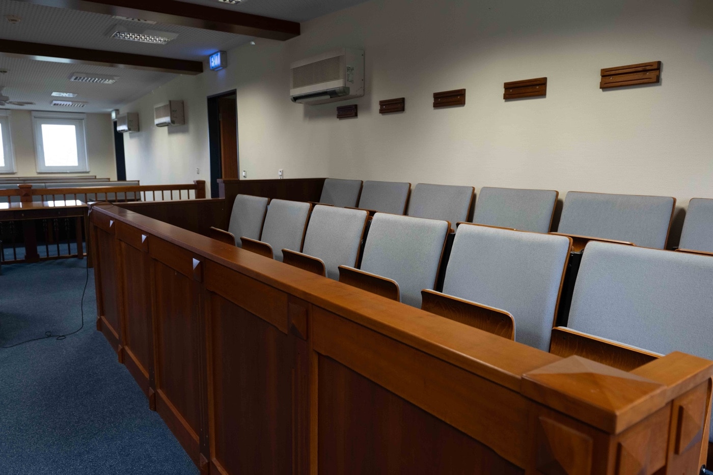 The photo shows an empty jury box in a traditional courtroom, with several wooden chairs lined up and ready for jurors to arrive. The view includes details like polished woodwork, a judge’s bench in the background, and subdued lighting, creating a serious and formal atmosphere. This image was taken ahead of a self-defense shooting trial, where the jury will be responsible for deciding if the defendant’s actions were justified under the law. The absence of jurors highlights the anticipation before a case begins and the importance of their role in evaluating evidence, including any firearms training records. The scene relates to courtroom proceedings, self-defense trials, and the critical job of the jury.