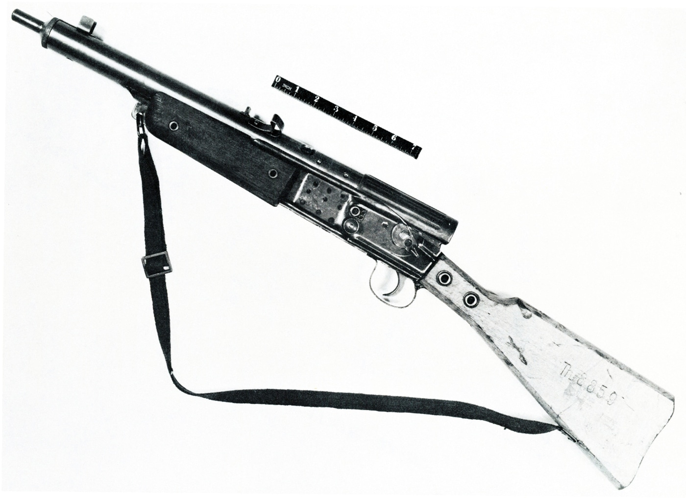 This image provides a full left-side profile of a Gustloff Volkssturmgewehr rifle, laid flat against a plain or neutral background for clear visibility. The rifle’s simple wooden buttstock, stamped sheet-metal receiver, fixed barrel, and curved magazine are all visible from this angle. The left-side controls, safety lever, and basic trigger group are identifiable, illustrating the rifle’s straightforward and utilitarian layout. Welding seams along the receiver and minimal finishing details reflect the rifle’s emergency, cost-driven manufacturing process. The sights are fixed and non-adjustable, further underscoring the design’s simplicity. This perspective allows for detailed examination of the overall proportions and construction techniques used in the Volkssturmgewehr. The image is suitable for reference in articles or technical documents focused on late-war German small arms. The photo captures the rifle as it would have appeared to a user or armorer during World War II.