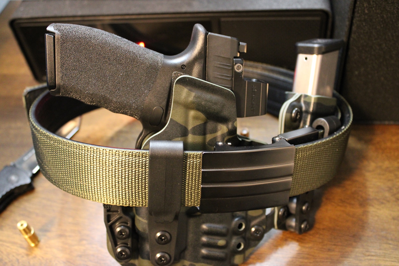 A close-up view shows a rigid Kore Essentials concealed carry belt threaded through the loops of a pair of jeans. The sturdy belt is designed for everyday carry, with a reinforced core and a slim, low-profile buckle that holds an IWB holster firmly in place. The photo highlights how a purpose-built gun belt prevents shifting or rising of the holster during the draw process. The wearer’s shirt is tucked slightly to reveal the belt and part of the holster clip, emphasizing functional setup. This image demonstrates why choosing a supportive EDC belt is critical for secure and effective concealed carry.