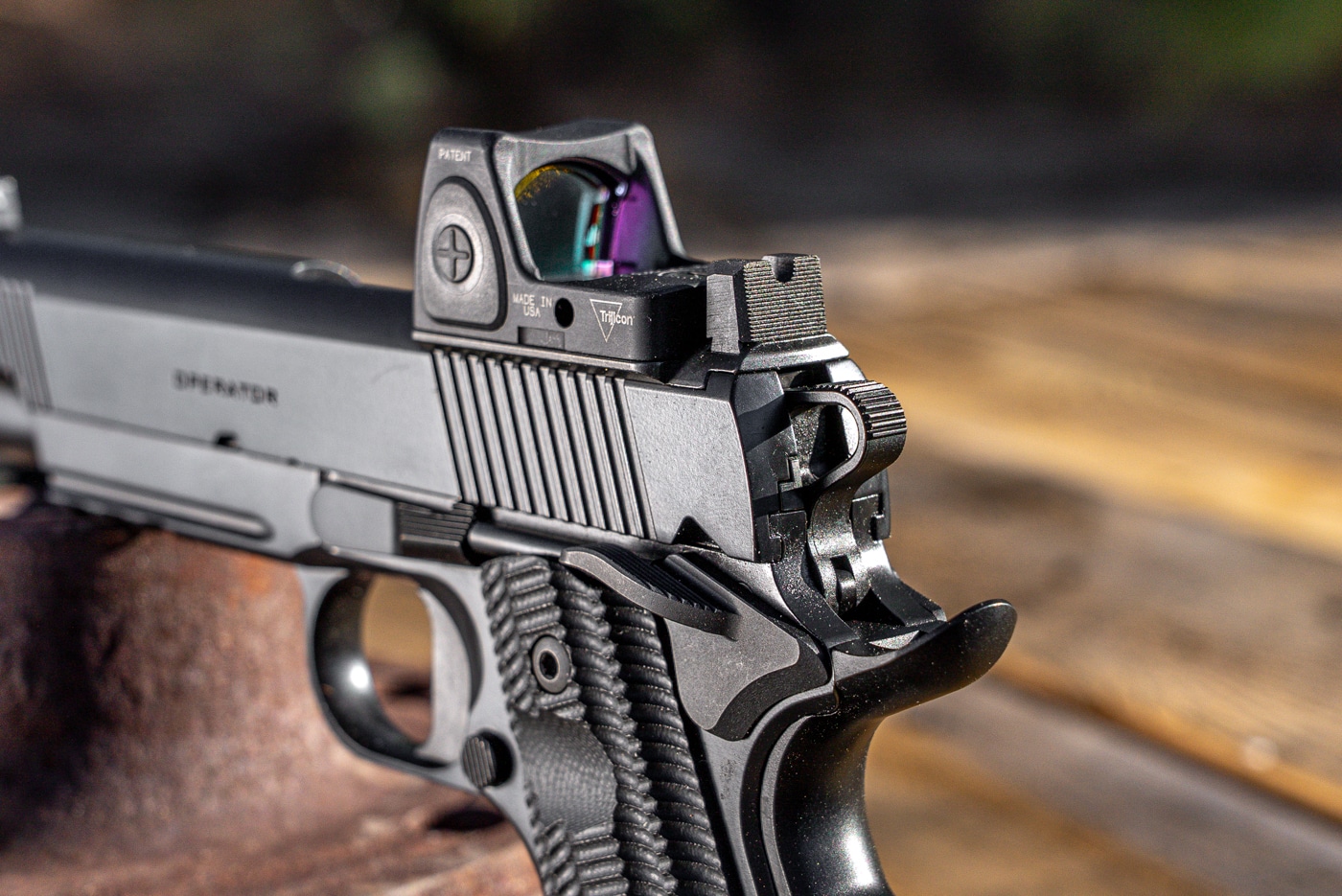 Close-up image of the rear portion of a Springfield Armory 1911 Operator AOS Threaded .45 ACP. The photo focuses on the installed red dot optic, which is mounted via the Agency Optic System (AOS) plate, and the suppressor-height rear sight. The tall rear sight is positioned to allow co-witnessing through the optic, providing a backup aiming option if needed. The Cerakote finish and detailed machining on the slide are clearly visible. The rear serrations and optic mounting hardware are easy to see. No other objects or hands are present; attention is centered on the pistol’s sighting features.