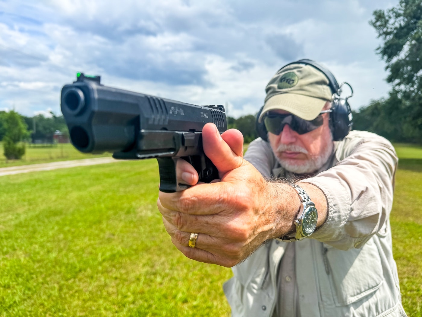 The image shows a shooter on the range, focused intently on the process of training trigger control. The shooter’s finger is positioned properly on the trigger, with attention paid to smooth, deliberate movement. The gun is held in a textbook grip, and the shooter’s stance is balanced and ready. Protective gear like safety glasses and earmuffs are visible, indicating a safe, controlled environment. The background includes range elements, but the main subject is clearly the shooter’s hands and trigger finger. This photo reflects the importance of consistent, mindful trigger training as discussed by Massad Ayoob. The image can be used to illustrate various stages of the trigger press, from initial contact to the break. The setting and posture reinforce the article’s focus on foundational shooting skills.