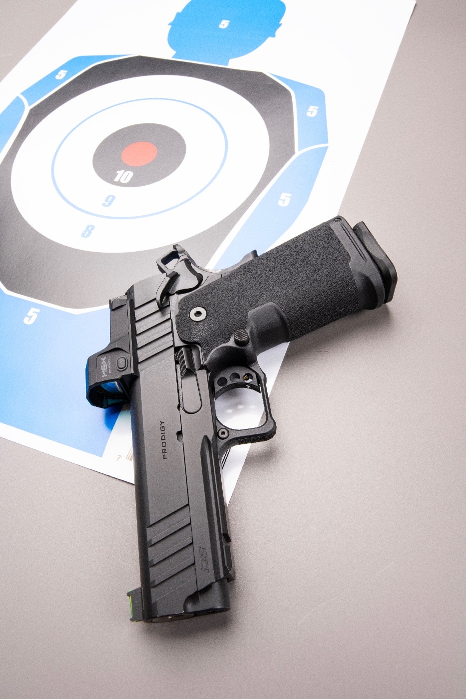 A Springfield Armory pistol is placed on a shooting bench beside a paper target filled with visible shot holes, illustrating the results of recent practice. The target features clearly marked hit zones, commonly used for self-defense and accuracy drills at public shooting ranges. The pistol is unloaded and positioned with the slide locked back for safety, in compliance with range rules. The simple setup emphasizes the basics of pistol training, including evaluating shot placement and tracking improvement. This image reflects the real-world tools and results of structured range sessions. The focus is on safe gun handling, target analysis, and effective practice routines. The photo supports content about public range etiquette, handgun selection, and skill-building drills.
