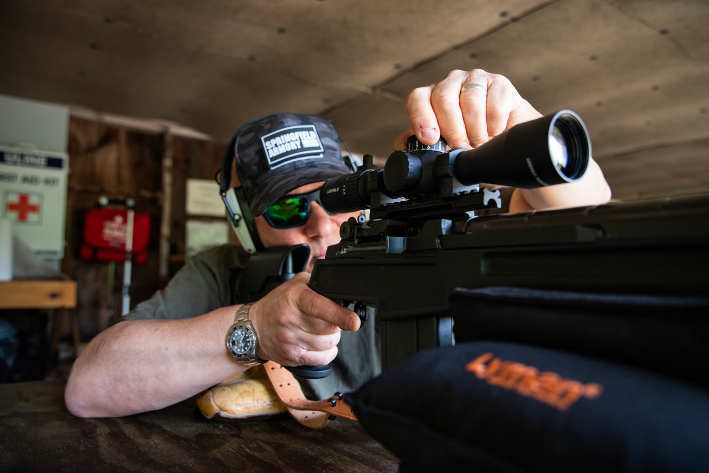 Photo of the author seated at a shooting bench, making adjustments to the elevation turret on the Leupold Mark 4HD 1.5-10x scope. The author’s hand is on the turret, showing how the controls are manipulated during use. The rifle is supported on a bench rest, and range gear is visible in the background. This image demonstrates real-world scope adjustments, such as zeroing or dialing for distance. The scene highlights the user-friendly nature of the Mark 4HD turrets and practical use during range sessions.
