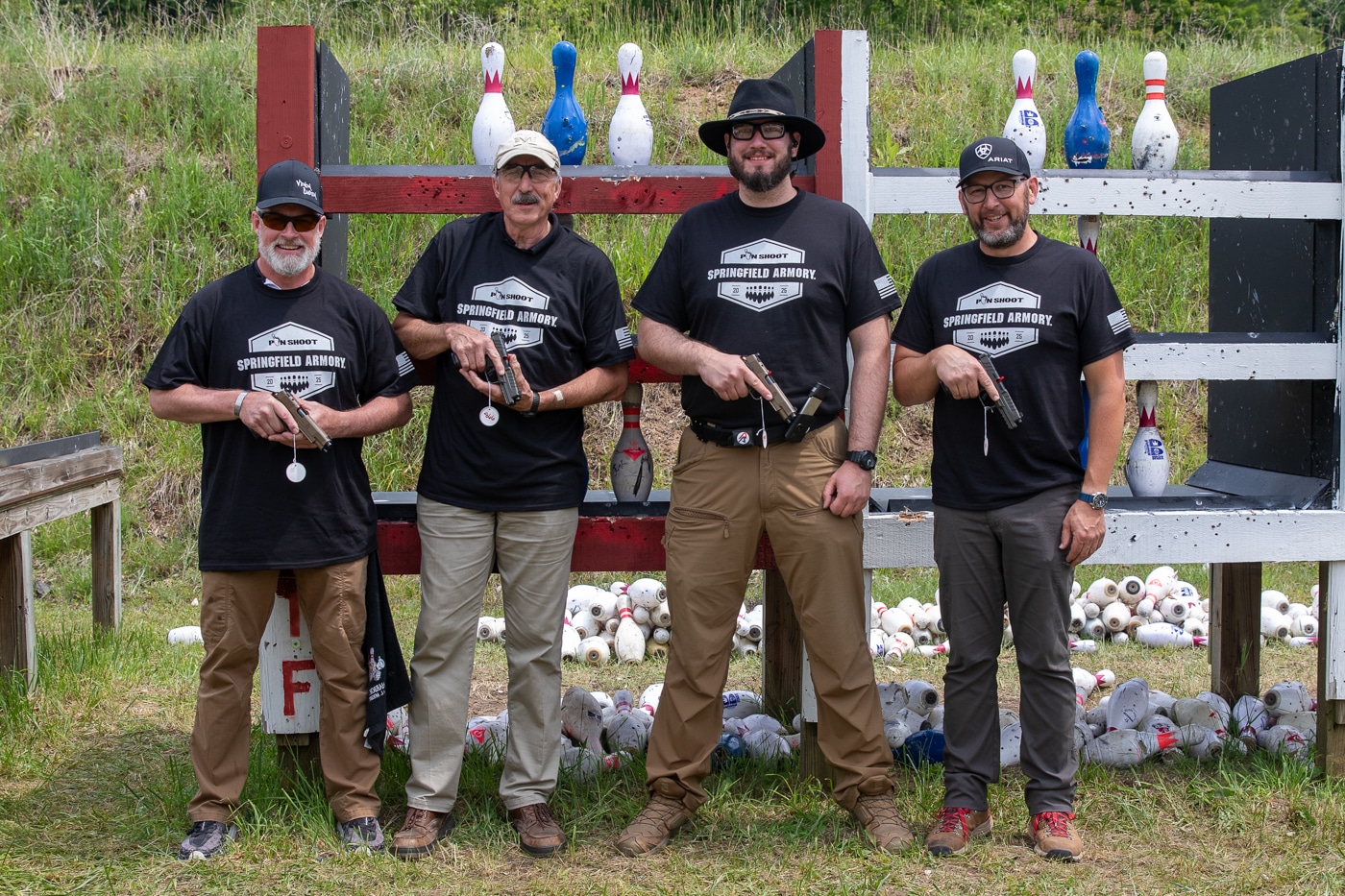 The winners of the 2025 Springfield Armory Shootoff stand together in a group photograph, each holding a Springfield Armory pistol received as an award. From left to right are Phil Farr, Patrick Sweeney, Ryan Rex, and David Alexander, all key competitors in the event. The men are smiling and wearing casual or event-branded attire, holding their firearms in front of them. The background shows an outdoor range or match setting. This image emphasizes the achievement and excitement of the winners after the competition. The group represents both OSS and Master Blaster category champions. Their presence and the prizes connect directly to the article’s coverage of the Springfield Armory Shootoff.
