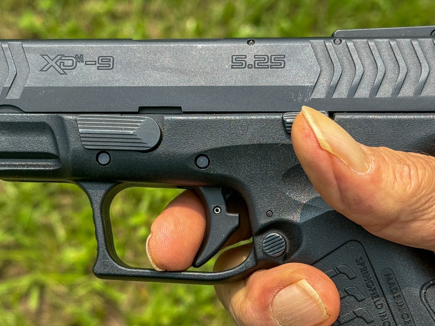 The close-up photo shows a shooter’s hand gripping a semi-automatic pistol, with the index finger in constant contact with the trigger as it is allowed to return fully forward to the reset position. The finger remains gently pressed against the trigger face, never breaking contact, illustrating the trigger weld technique explained in the article. The details of the grip, trigger, and finger position are sharp and clear, highlighting the mechanics of this method. The gun’s frame and trigger guard are visible, with the background blurred to emphasize the hands and trigger area. This visual directly supports Massad Ayoob’s discussion of the “middle ground” between trigger slap and riding the sear, balancing reset with control. The photo helps readers understand what continuous trigger contact should look like during practical or defensive shooting. The image is suitable for demonstrating proper trigger technique in instructional material.