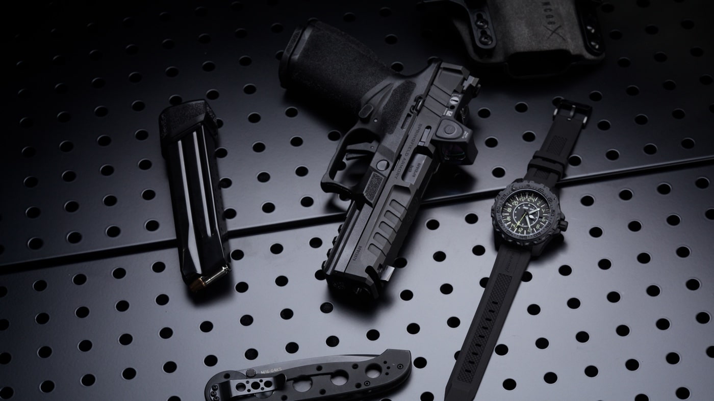This photo features the Springfield Armory Echelon pistol next to an ArmourLite watch, both arranged on a textured, tactical-style surface. The Echelon is angled to show its sleek, modern slide cuts, aggressive grip texture, and accessory rail, while the ArmourLite watch sits nearby with its illuminated markers and tough case construction visible. The photo highlights the progressive engineering found in both the firearm and the watch, visually connecting the two brands’ focus on innovation and field performance. No other accessories are present, allowing viewers to focus on the product details. The lighting is crisp, drawing out the surface textures and making the scene feel contemporary and purposeful. This image is used in the article to underline how ArmourLite timepieces fit naturally alongside the newest Springfield Armory models, especially for readers interested in the latest tactical gear.