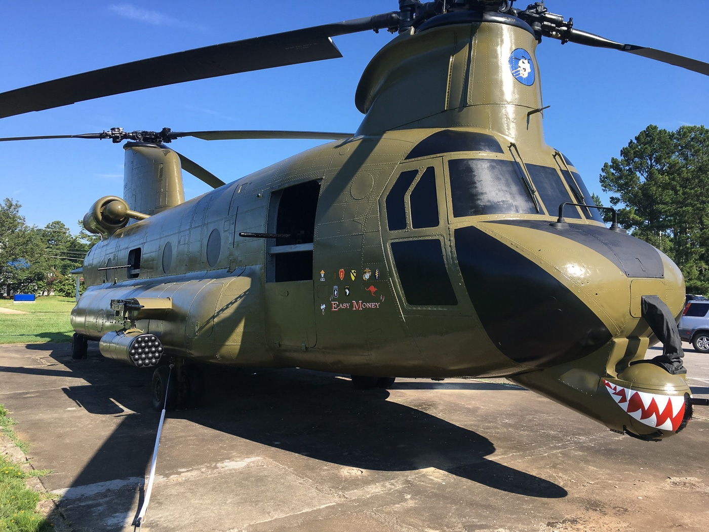 The photograph shows the fully restored ACH-47A Easy Money, the last surviving example of the U.S. Army’s “Guns-A-Go-Go” Chinook gunships. It is displayed outdoors at Fort Rucker, Alabama, painted in authentic Vietnam War-era olive drab with original markings. The helicopter retains its complete weapons fit, including sponson-mounted rocket pods, 20mm cannons, and multiple machine gun mounts. This aircraft served in combat during the Vietnam War before being retired and later restored for public display. The restoration includes historically accurate paint, stenciling, and structural repairs. The display serves as both a historical artifact and an educational tool for visitors. The image captures the helicopter from the side, showing its size, armament, and preserved condition.