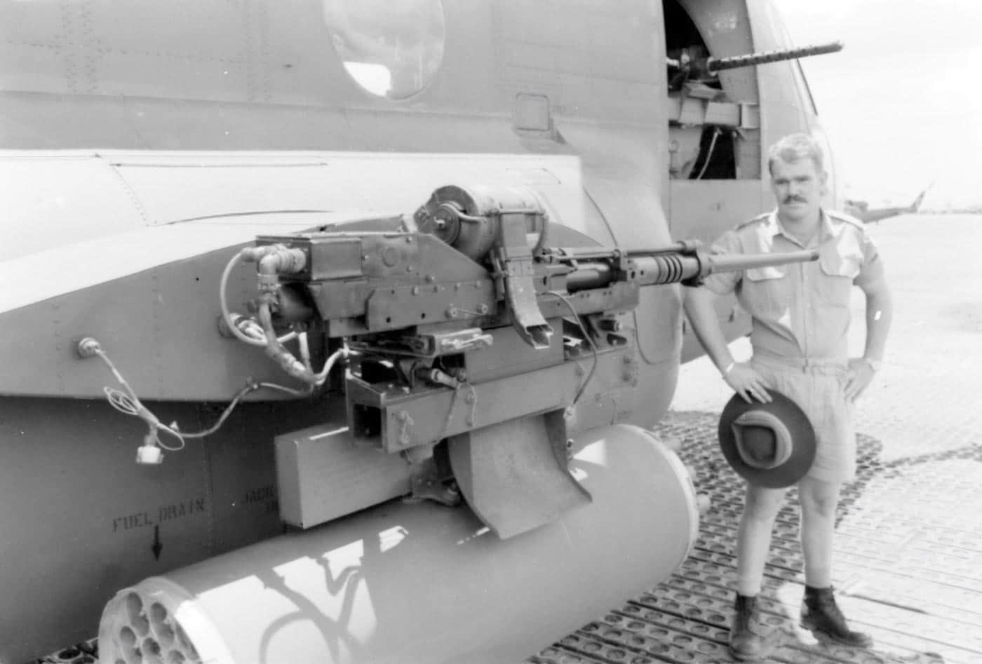 The photograph shows an Australian soldier standing beside the ACH-47A Birth Control gunship during the Vietnam War. The soldier appears to be examining the helicopter’s weapons sponson, which houses a combination of rocket pods and cannons. Birth Control was part of the U.S. Army’s limited Guns-A-Go-Go program, which modified the CH-47 Chinook into a heavily armed assault platform. The ACH-47A carried grenade launchers, 20mm cannons, rocket launchers, and multiple machine guns for close air support. This image captures a moment of allied cooperation, as Australian and American forces frequently operated in overlapping areas of Vietnam. The helicopter is painted in standard olive drab with unit markings visible on the fuselage. Details of the sponson-mounted armament and armor plating can be clearly seen.